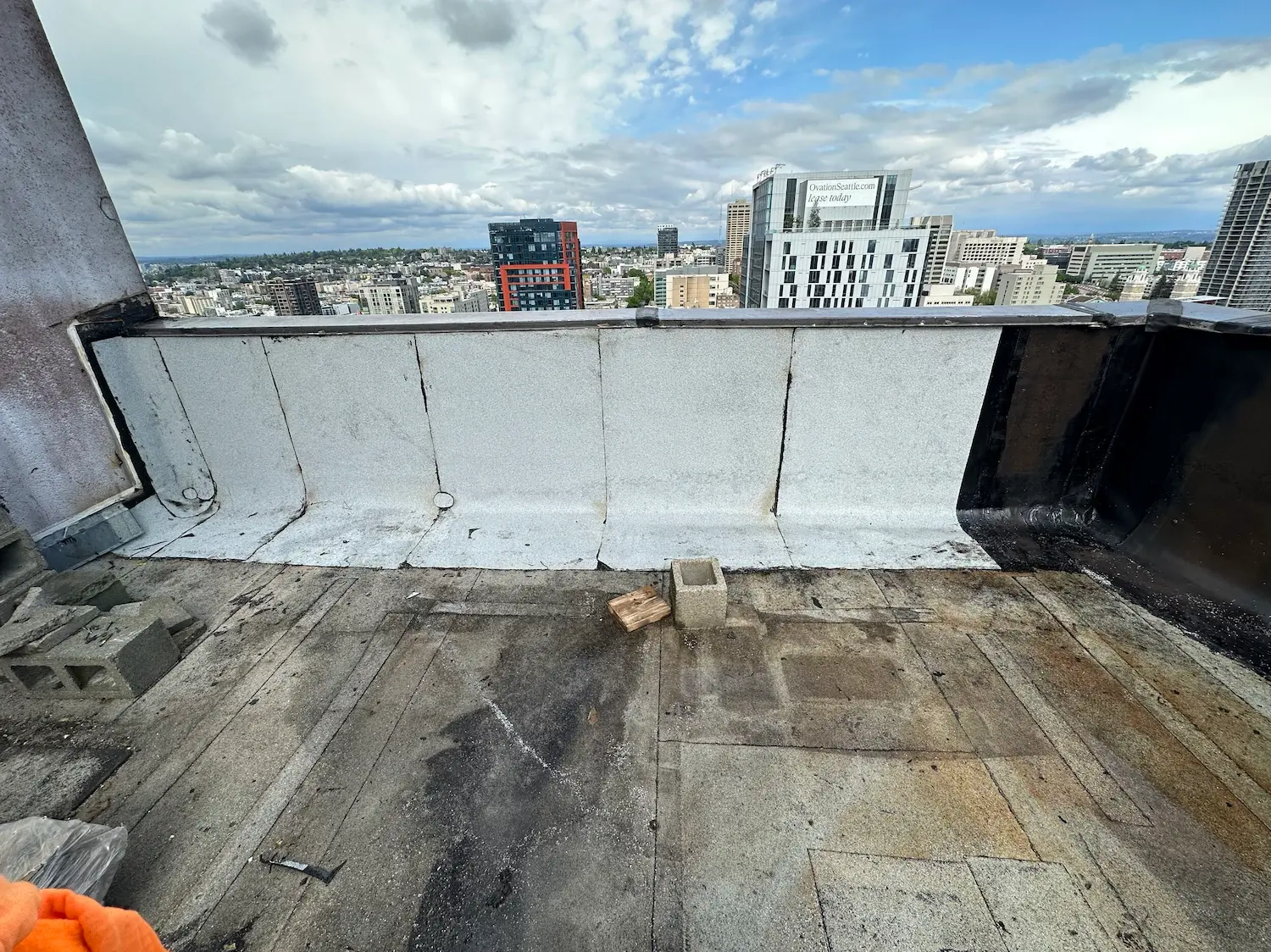 Partially restored flat commercial roof in Seattle with new granulated cap sheet installed on parapet walls, showing in-progress waterproofing work and urban skyline in background.