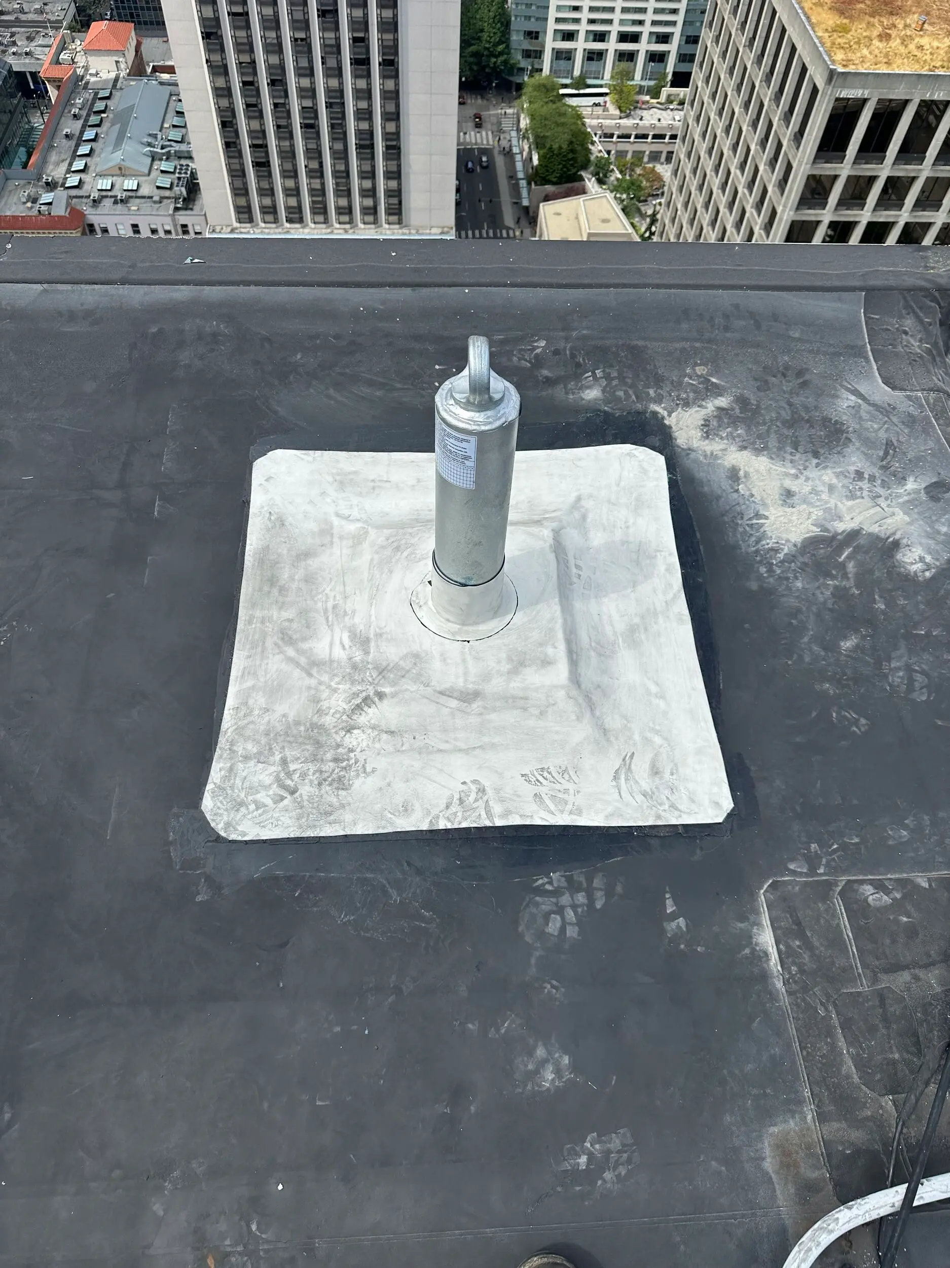 Newly installed rooftop safety anchor sealed into single-ply membrane on a high-rise flat roof in downtown Seattle, ensuring fall protection system compliance.