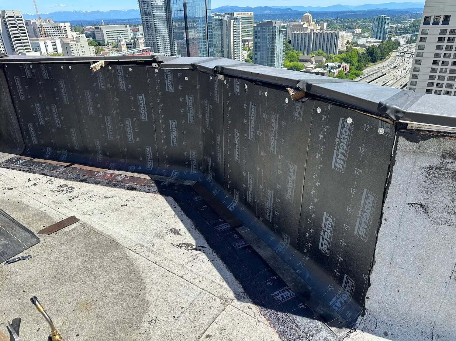 Parapet wall preparation on a high-rise flat roof in Seattle, featuring newly installed Polyglass self-adhered base sheet as part of a waterproofing system upgrade.