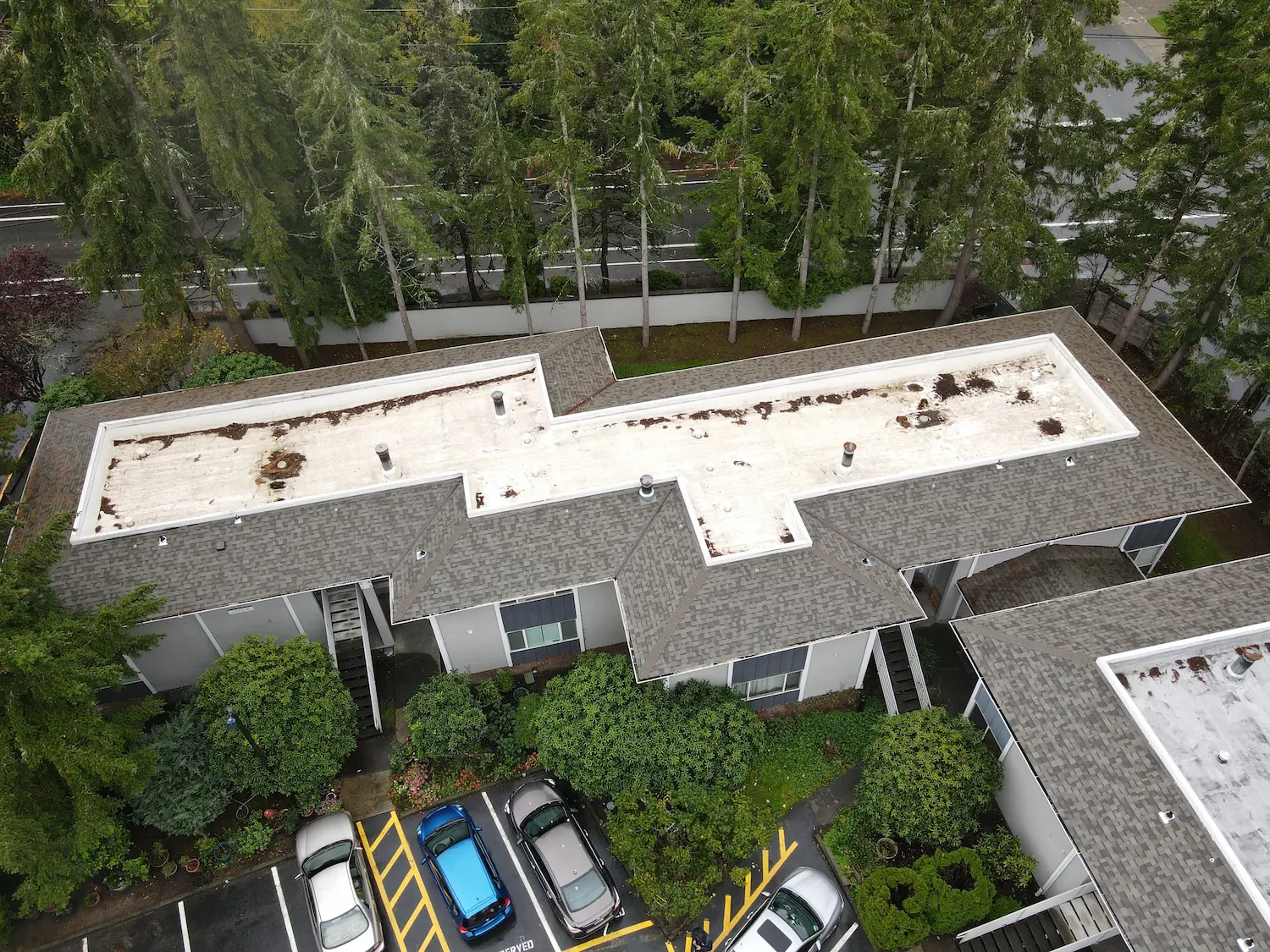 Aerial view of multi-family building with a flat roof showing signs of debris buildup, standing water stains, and aging membrane—indicating need for flat roof maintenance or restoration.