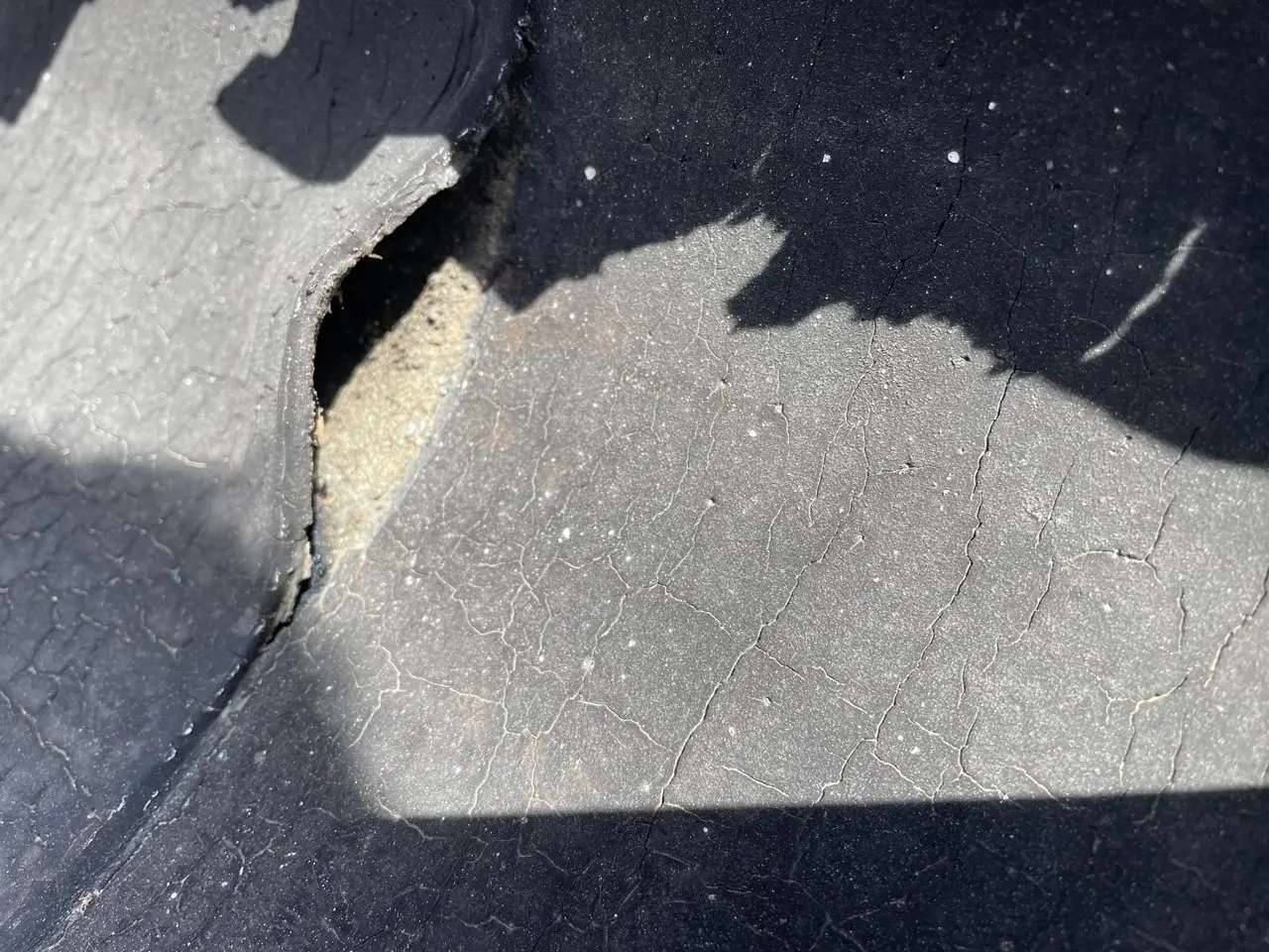 Cracked and torn flat roof membrane, exposing underlayment and risking water intrusion. Signs of aging, UV damage, and structural stress on the roofing surface, highlighting the need for roof repairs.