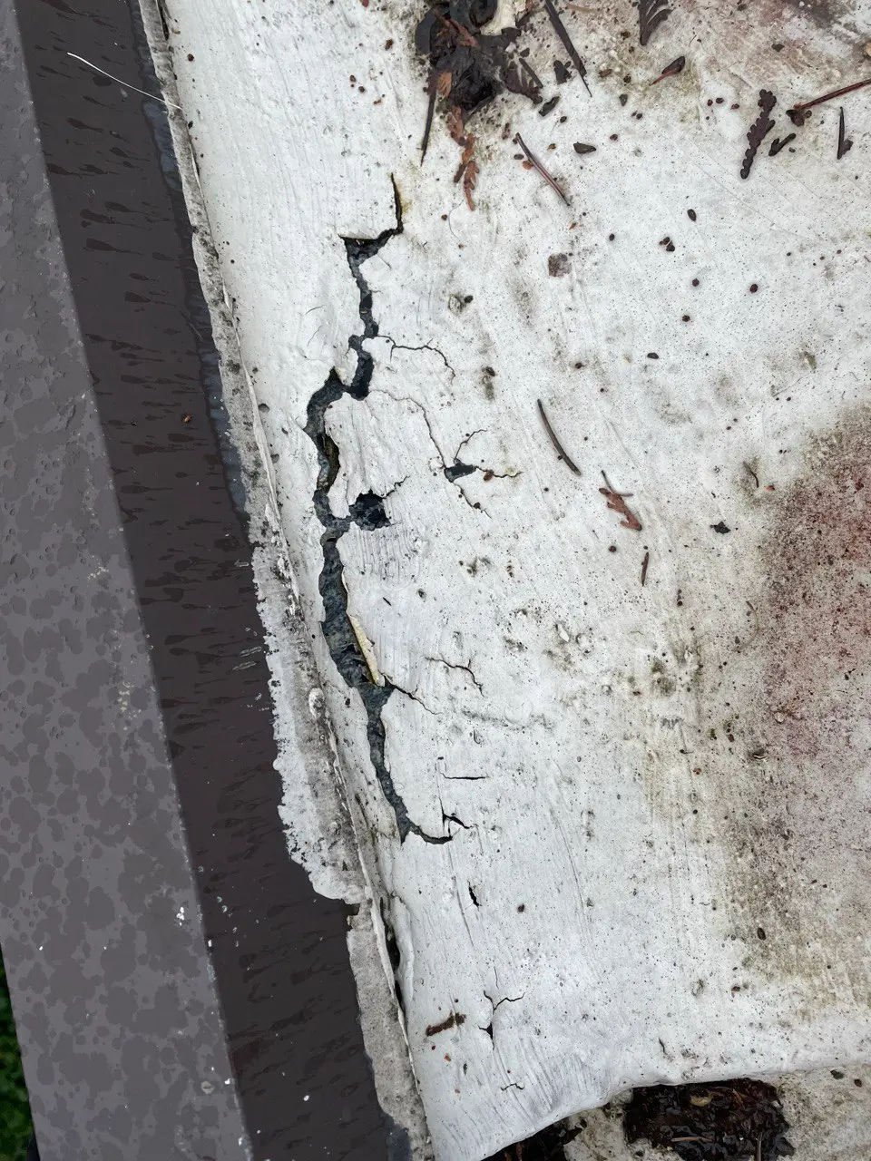 Cracks and weathering damage on flat roof edge, showing worn and deteriorated roofing material at risk of leaks and further structural issues.