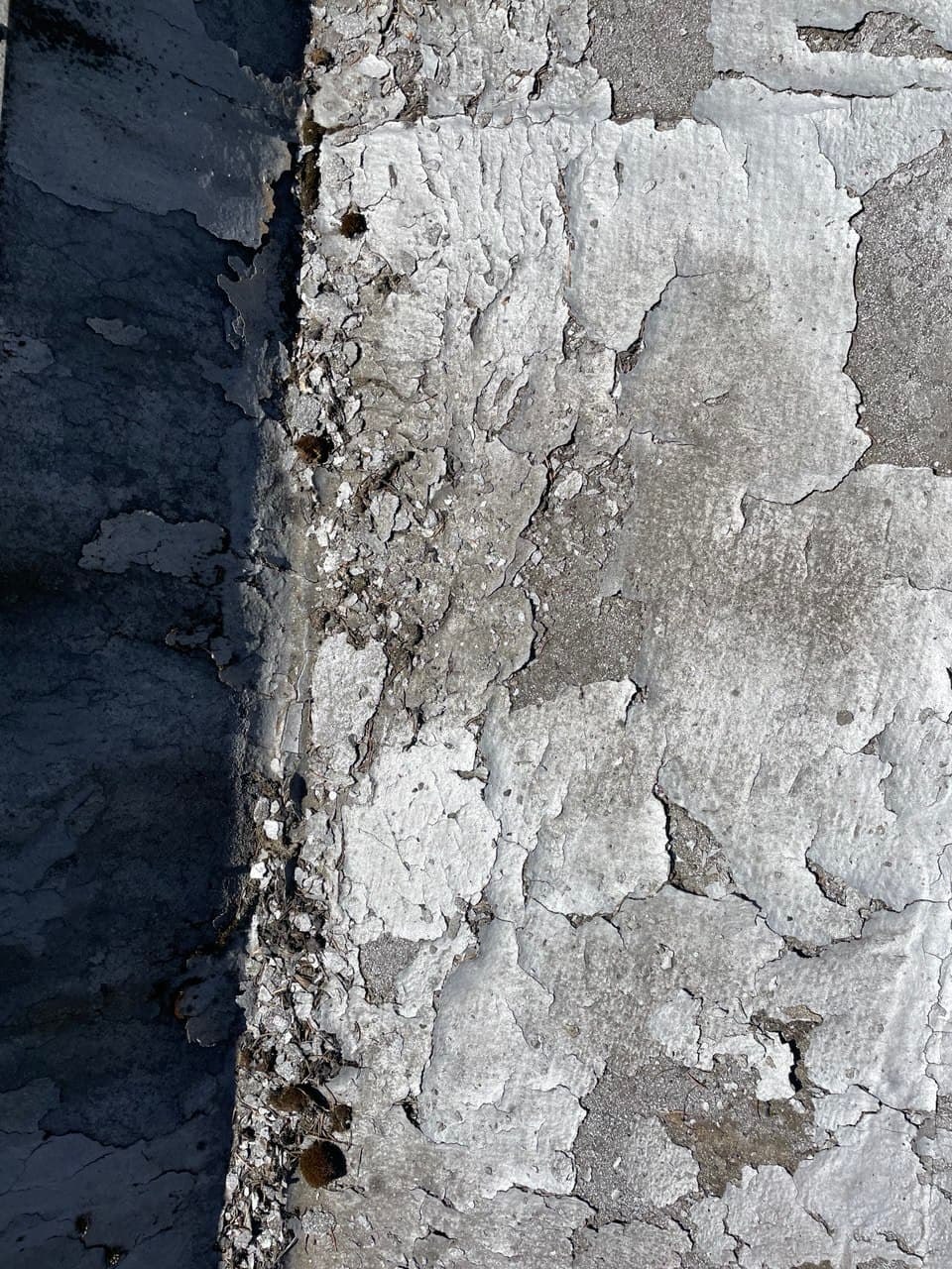 Old, weathered roofing surface with cracked and peeling layers, showing signs of advanced material degradation and age-related wear.