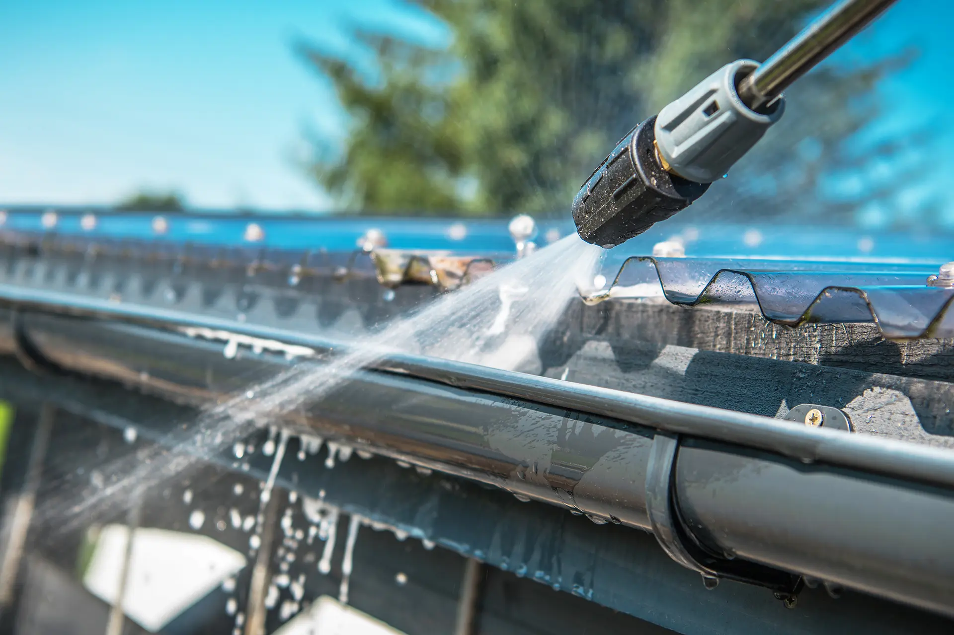 Close-up of pressure washing roof and gutter system — removing dirt, moss, and debris to improve drainage and extend roof life as part of seasonal maintenance.