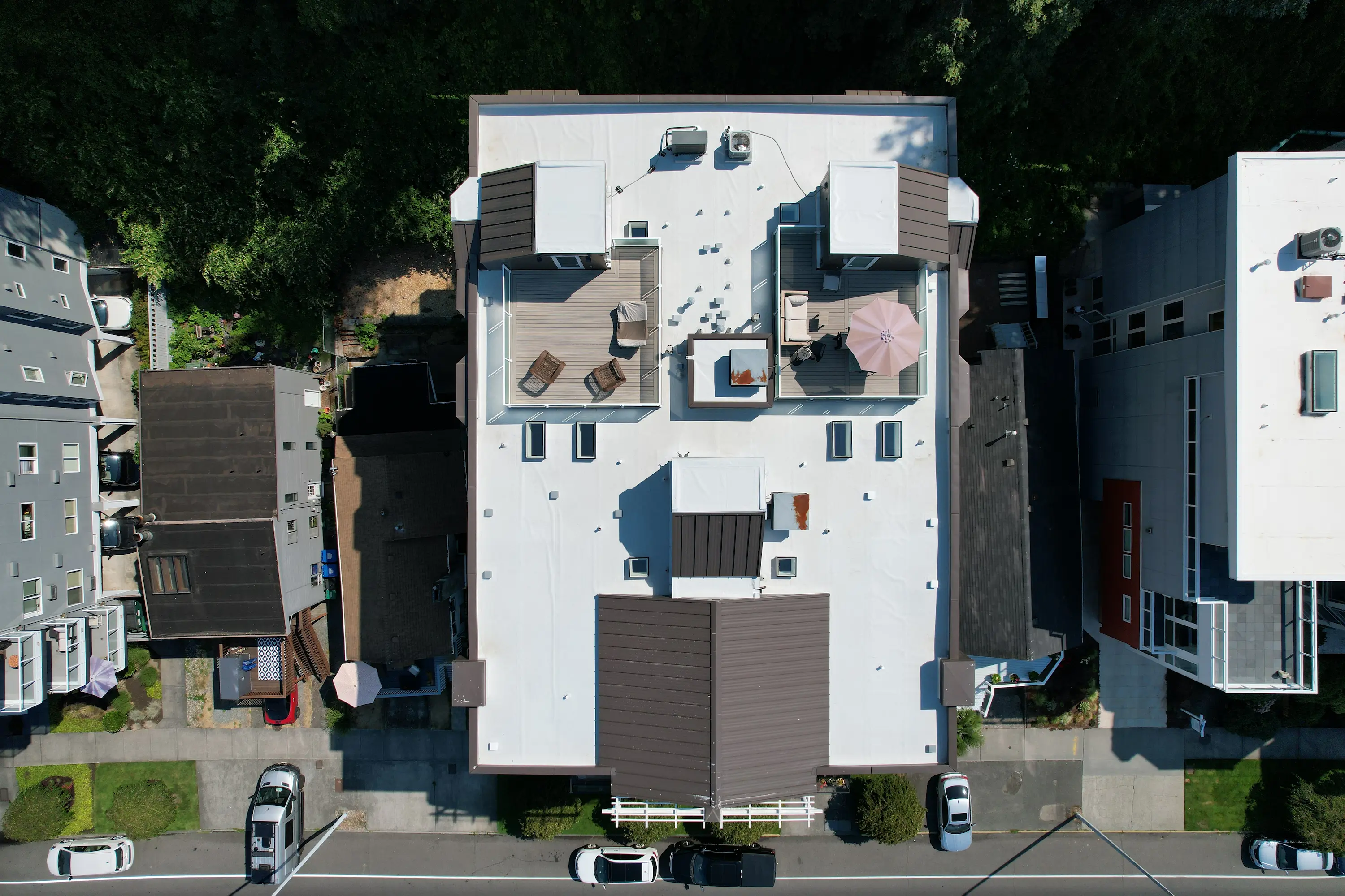 Aerial view of a newly installed white PVC flat roof with rooftop decks and modern finishes on a residential building in Seattle, energy-efficient, leak-proof flat roofing system by Flat Roof Pros.