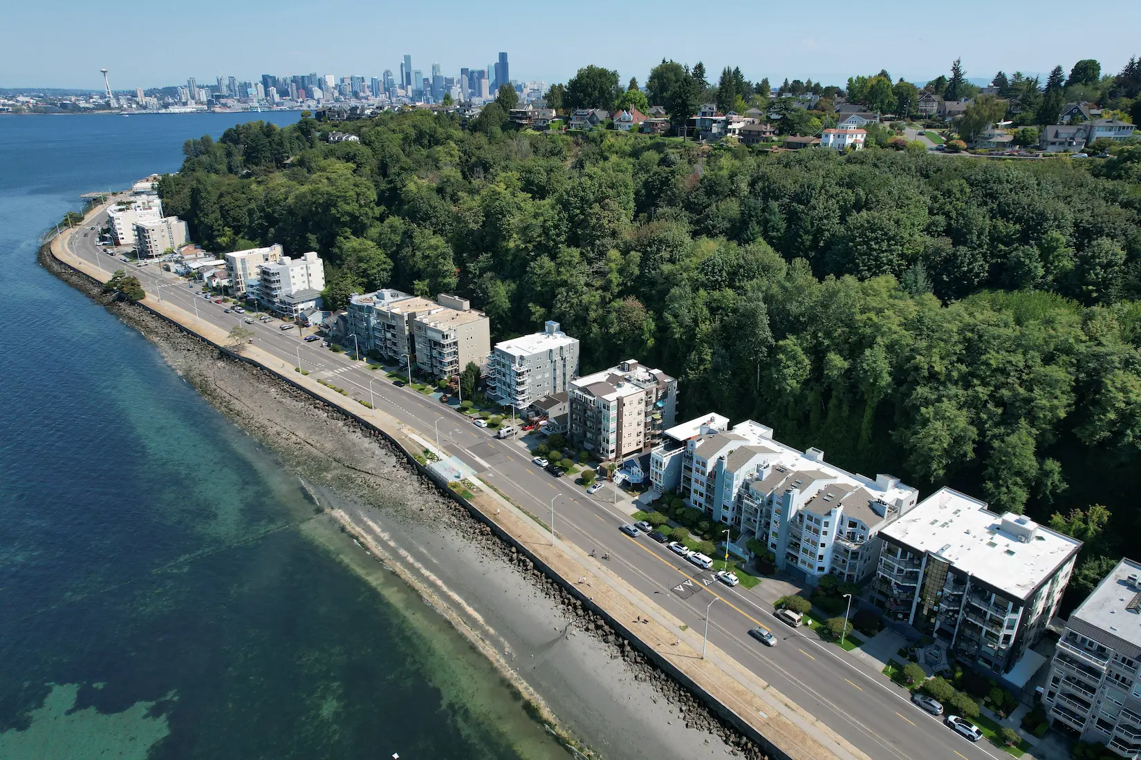 Aerial view of Alki Apartments in West Seattle showing a newly installed white GAF 80-mil TPO flat roofing system with skylights, coping, and rooftop HVAC units, surrounded by modern residential buildings and forest backdrop.