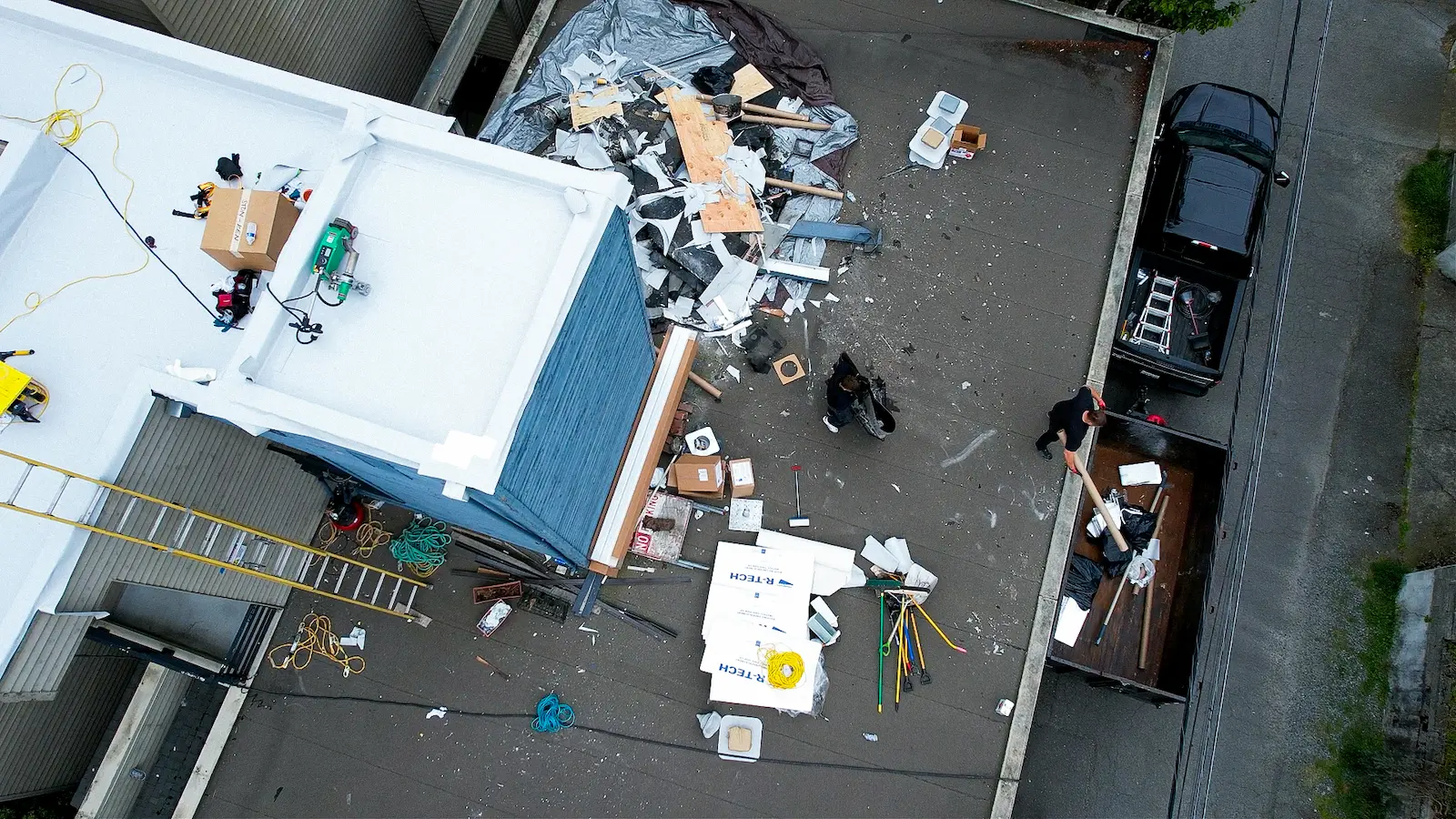 Flat Roof Pros NW tenant care: crew loading roof debris into a trailer, keeping entrances and parking clear during reroof.