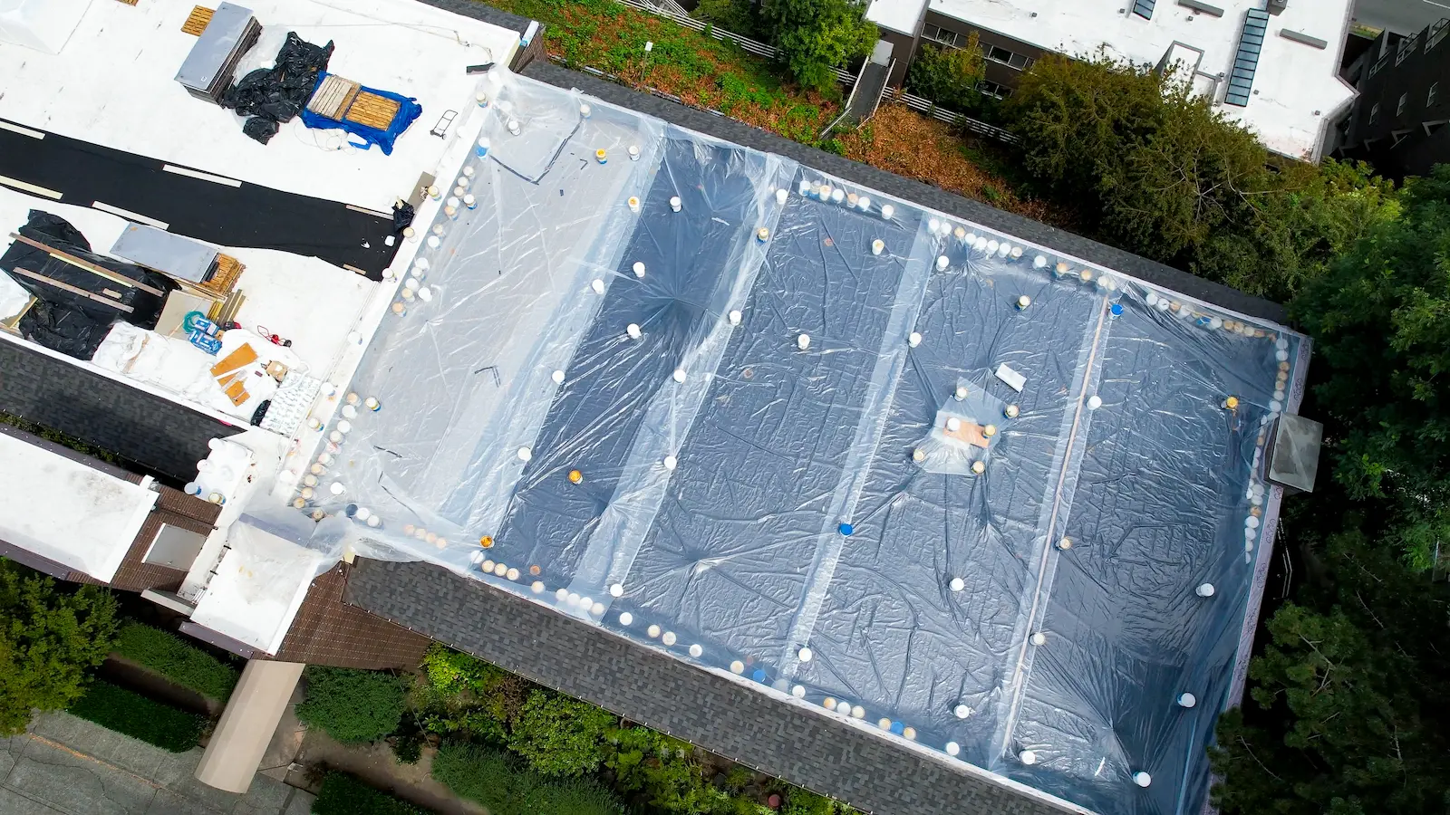 Flat Roof Pros NW end-of-day QC: phased roof sections under plastic, penetrations tarped and seams weighted to prevent leaks.