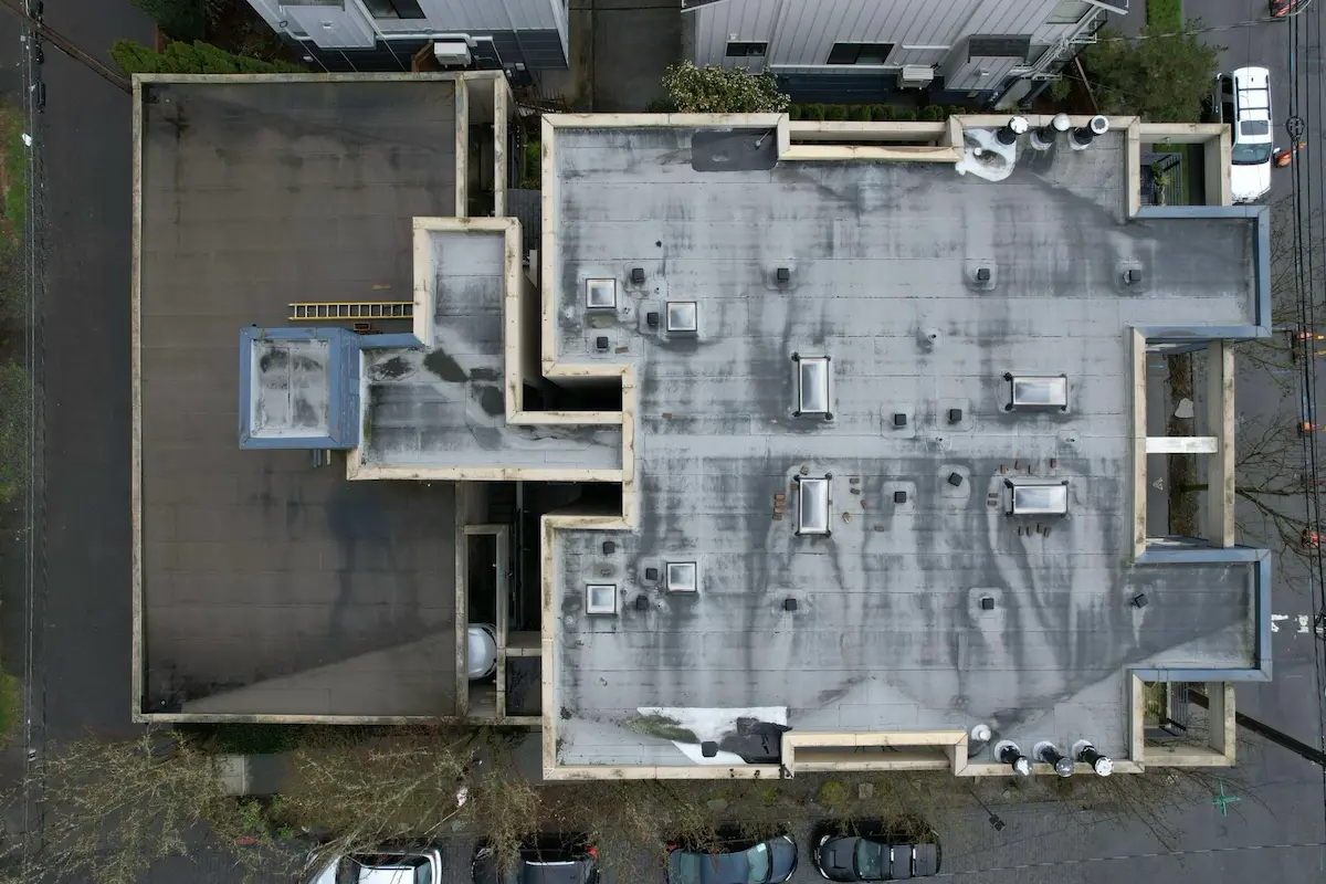 Top-down view of an aging apartment building roof in Seattle, highlighting worn membrane sections, ponding patterns, and multiple penetrations in need of replacement.