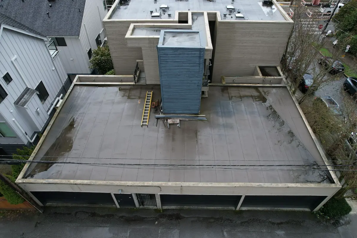 Drone image capturing the deteriorated condition of a low-slope roof on a multifamily property, with visible staining, standing water, and outdated flashing details.