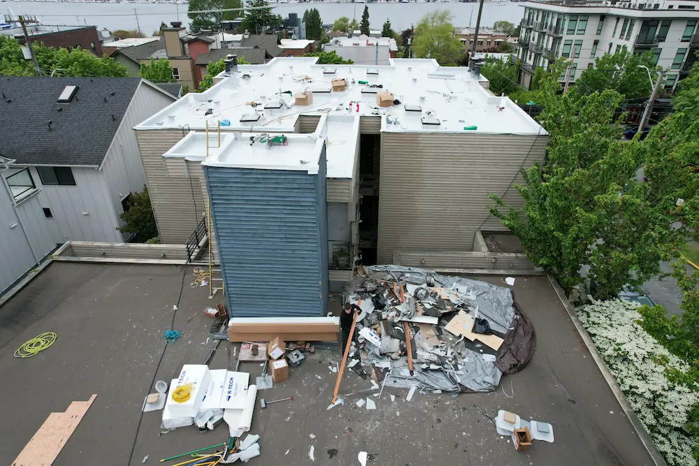 High-angle drone photo of an in-progress flat roof replacement, showing active installation and a controlled debris zone before daily cleanup.