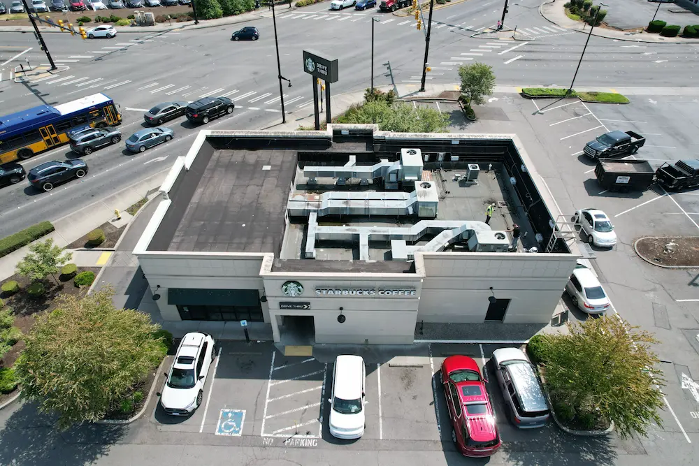 Aerial before-photo of a worn commercial flat roof on a Starbucks building in Washington State, showing aging membrane, exposed HVAC units, and areas needing repair.
