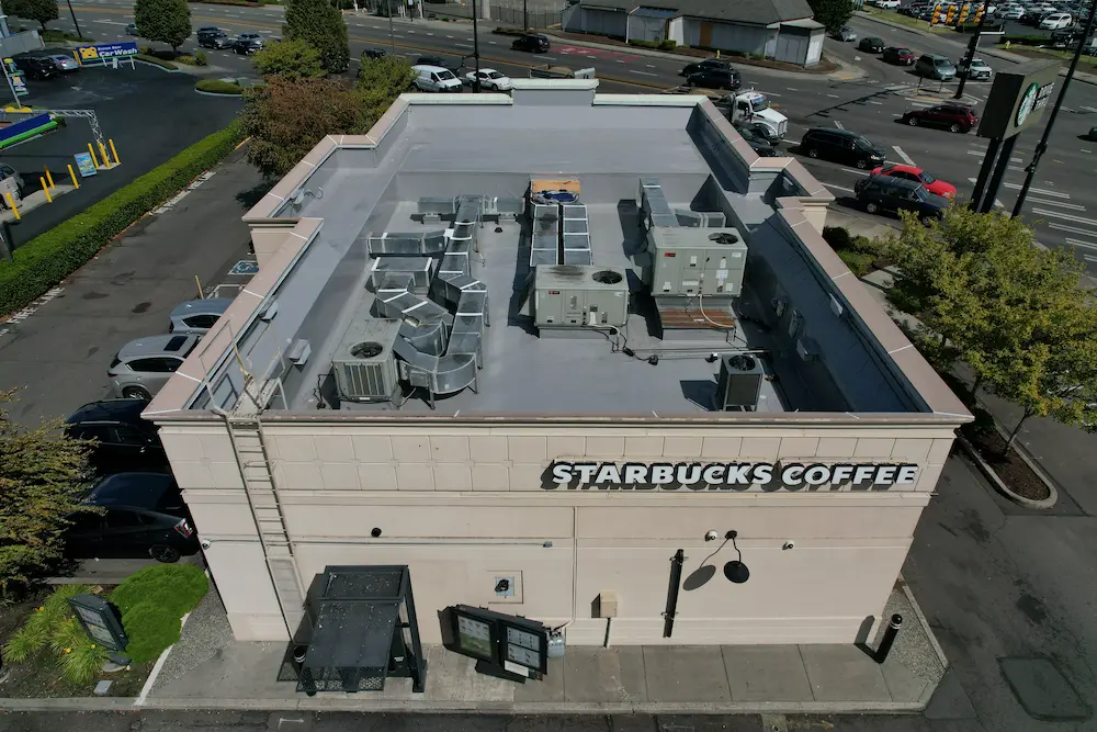 Aerial after-photo of a completed commercial flat roof restoration on a Starbucks in Washington State, featuring a clean, newly coated membrane and detailed waterproofing around all HVAC units and penetrations.
