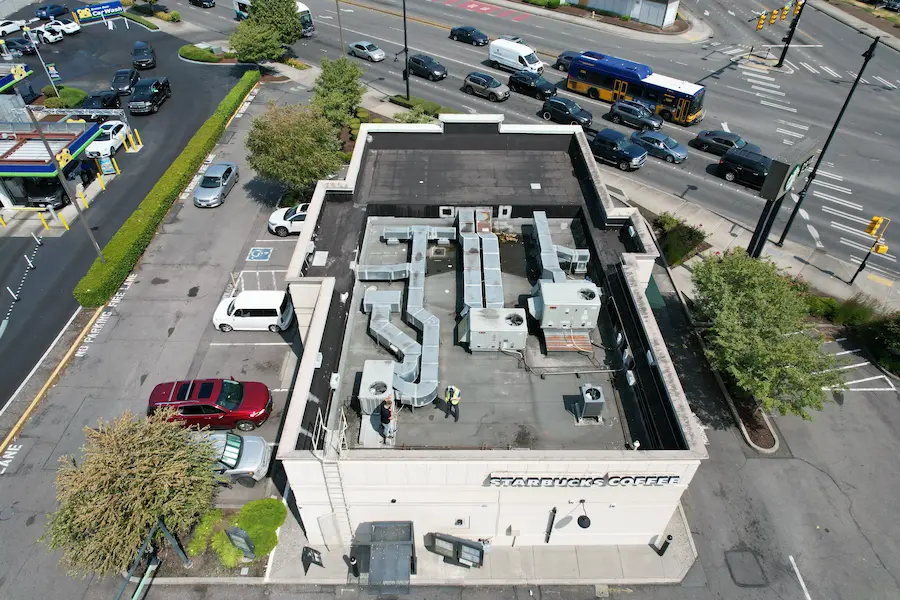 High-angle drone photo showing the original aging flat roof on a Starbucks building, with visible membrane wear and exposed mechanical ductwork prior to restoration.
