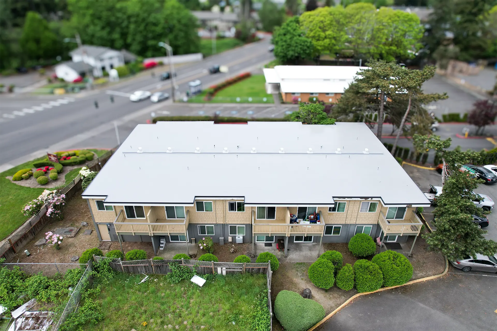 Angled aerial shot of a multifamily apartment roof after silicone restoration, showing clean membrane, new vents, and uniform waterproofing.