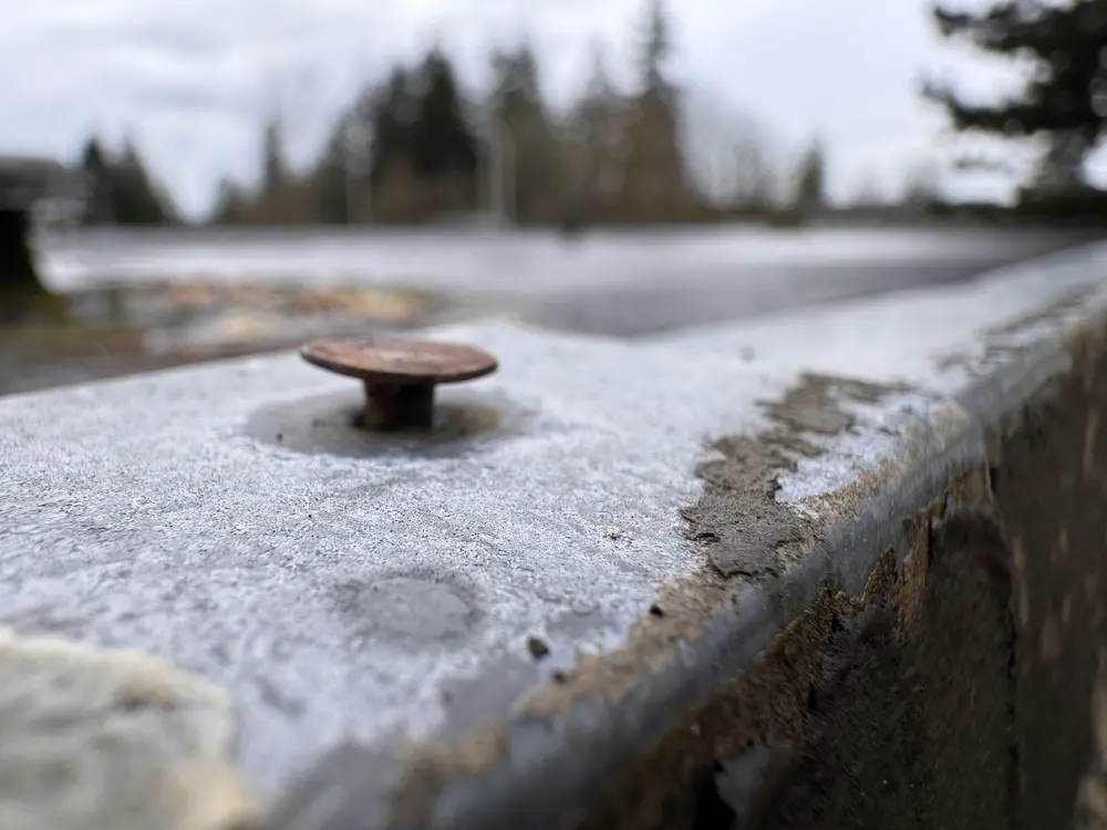 Close-up photo of a rusted exposed fastener on the roof edge, showing deterioration prior to replacement.