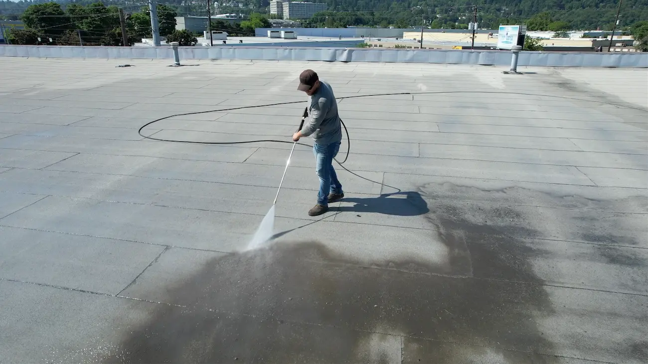 Technician pressure-washing the commercial flat roof to remove dirt and contaminants as part of preparation for the silicone restoration system.
