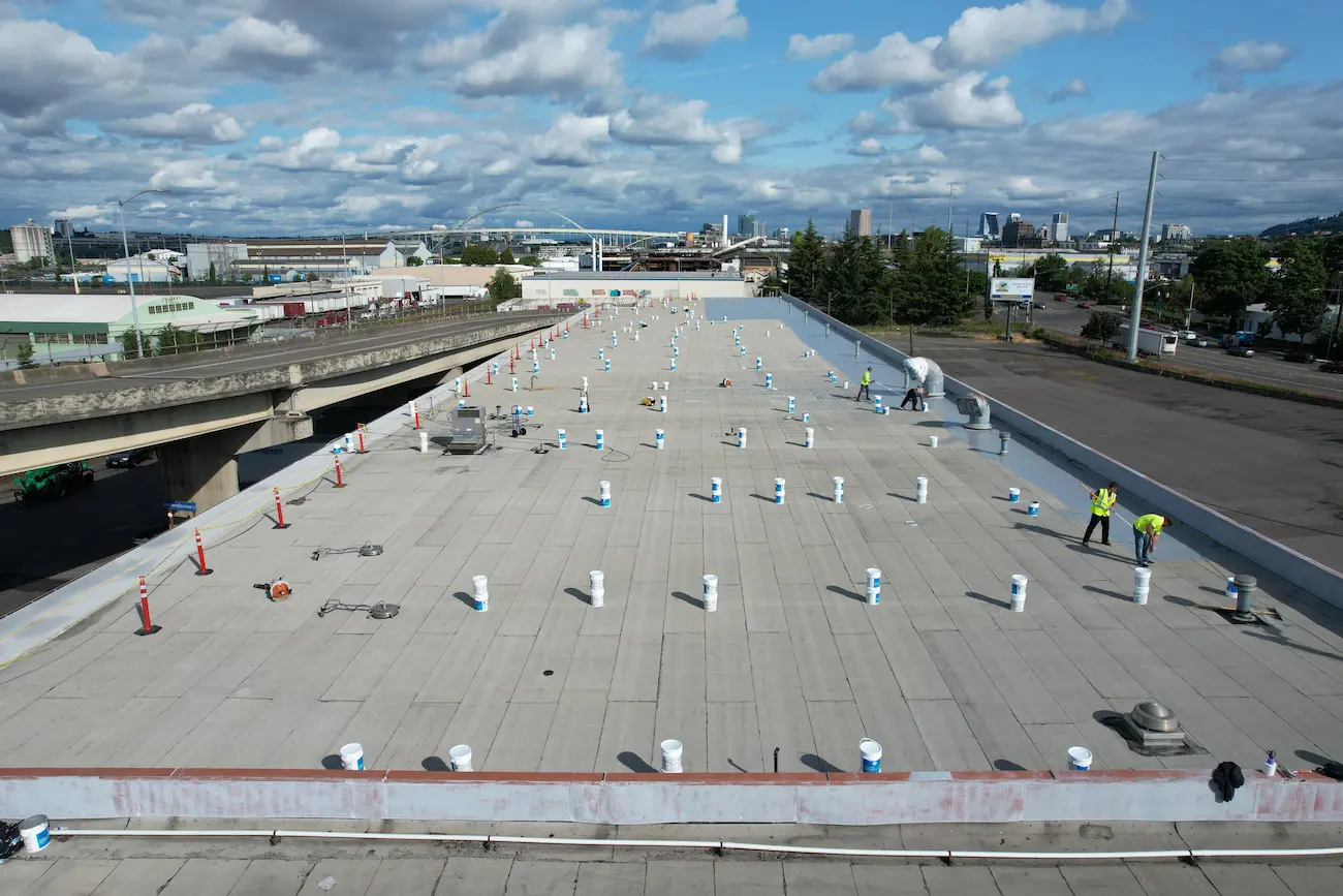 Wide drone view of the roof during preparation with buckets of silicone coating placed throughout and crew members Flat Roof Pros prepping seams and penetrations.
