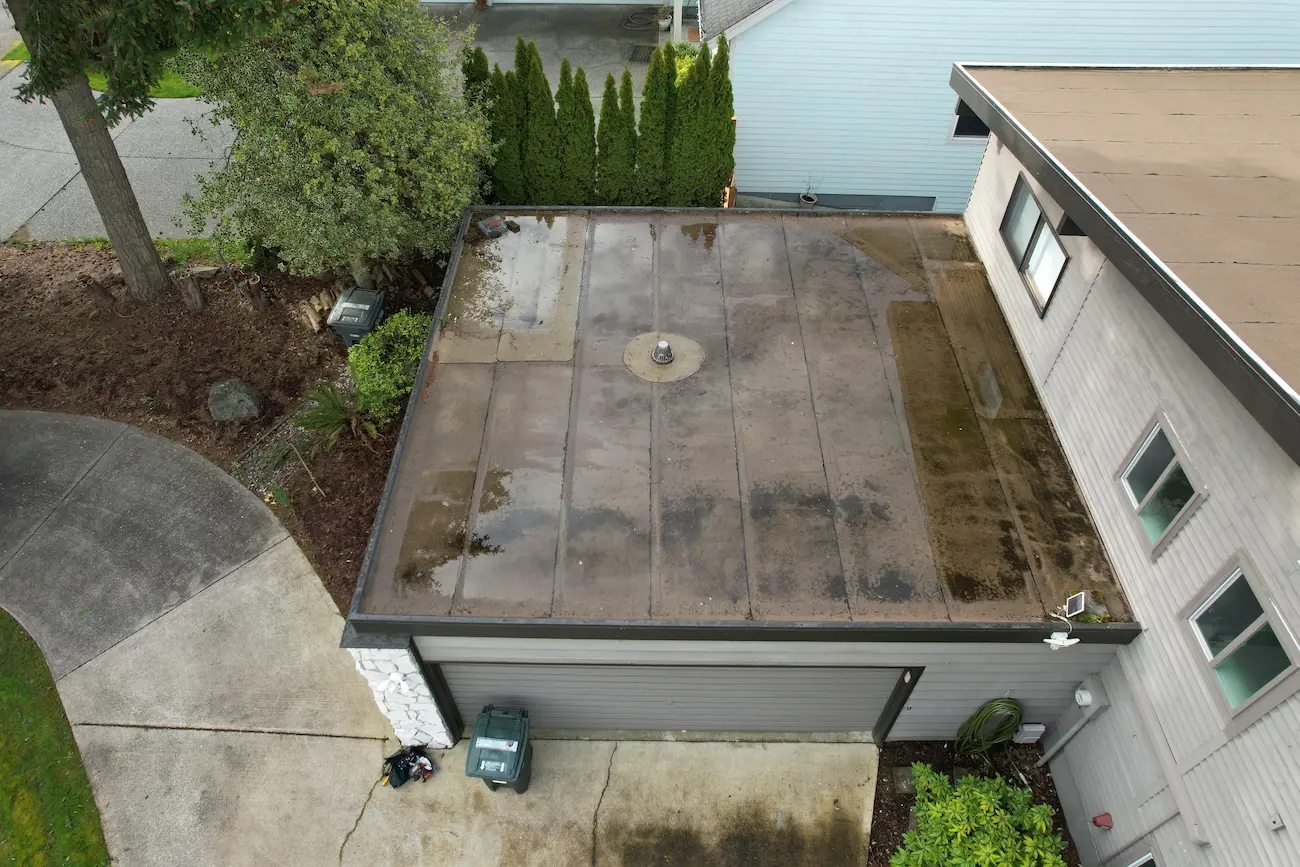 Garage flat roof with ponding water, membrane deterioration, and visible staining prior to full replacement.