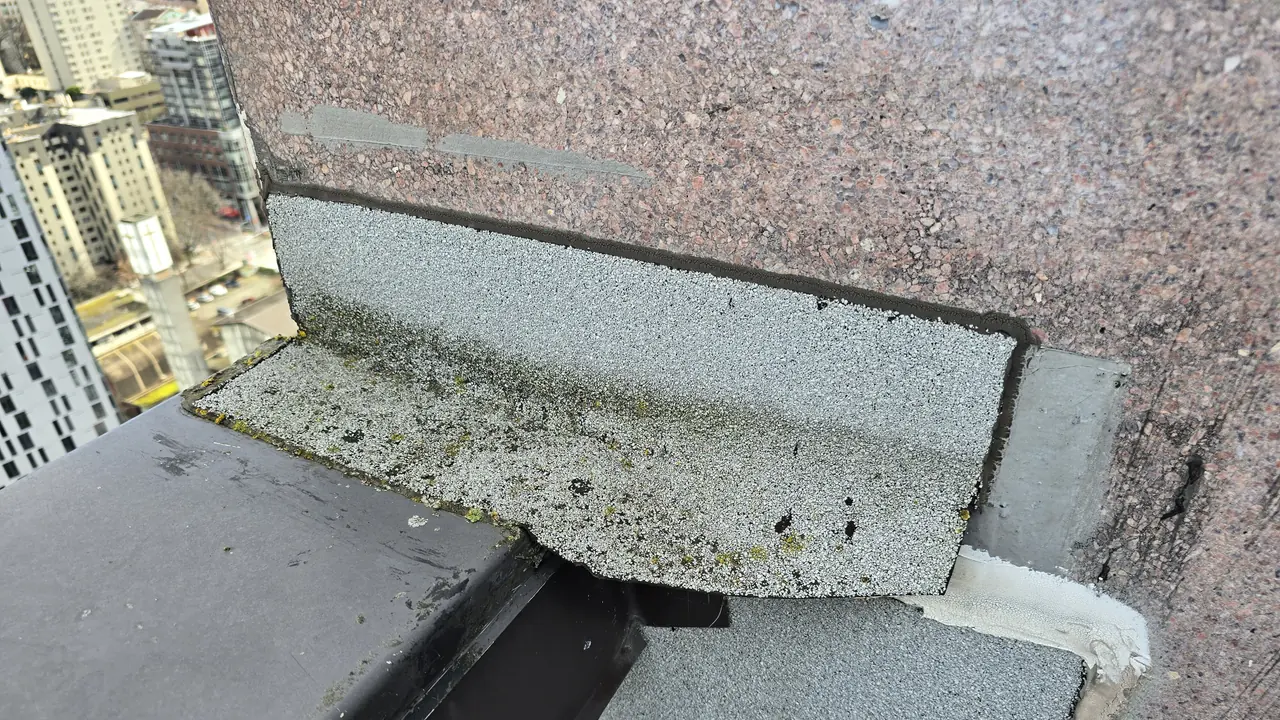 Flat-roof wall transition and flashing detail where water can enter and travel before appearing indoors.