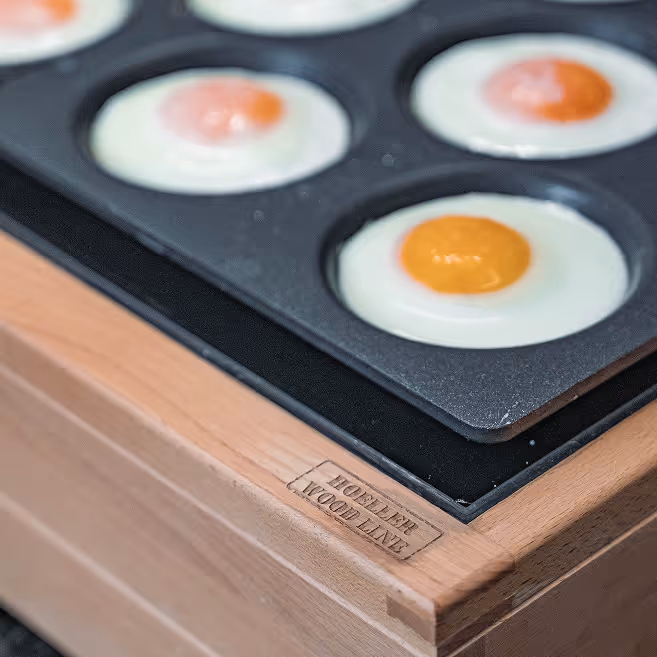 Kovová forma na pečení vajec nasazená na dřevěném podstavci s vyrytým nápisem Hoeller Wood Line.