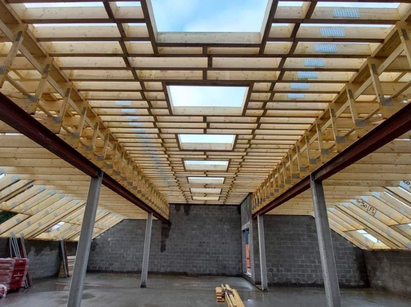 Charpente préfabriquée avec fermettes en bois et poutres en acier en cours de montage.