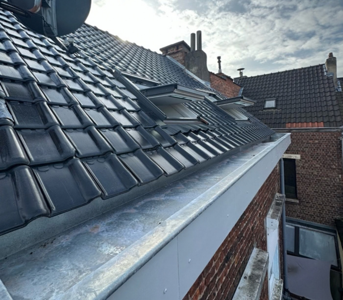 Nieuwe zinken bakgoot langs een dak met zwarte geglazuurde dakpannen, geplaatst door LFN Dakwerken.