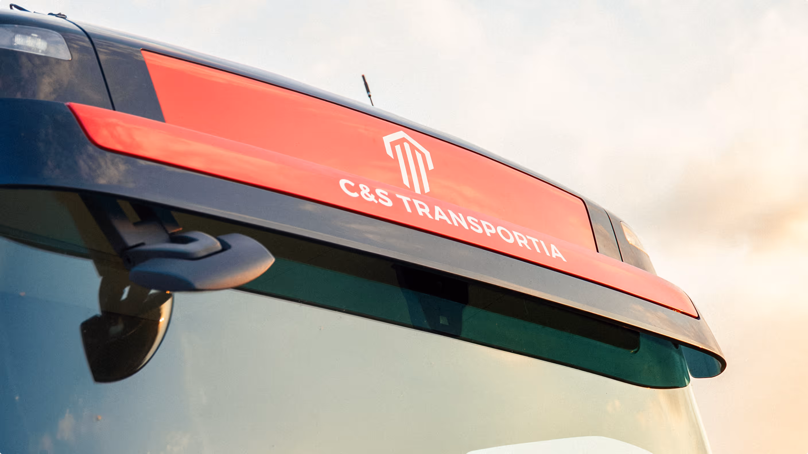 Detail na čelní část nákladního auta s červeným pruhem a logem C&S Transportia.