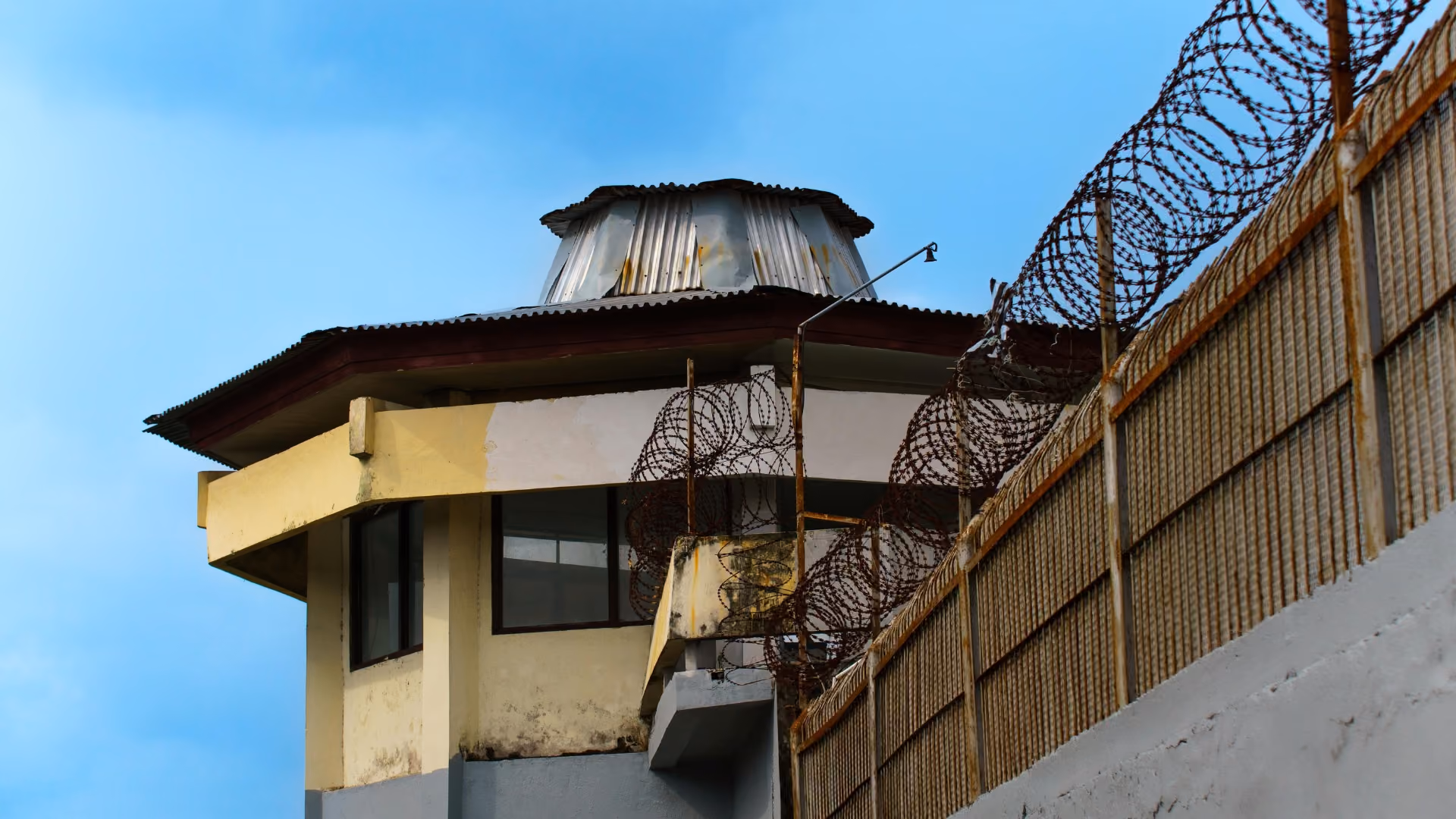 Guard tower with barbed wire fence against a blue sky background.