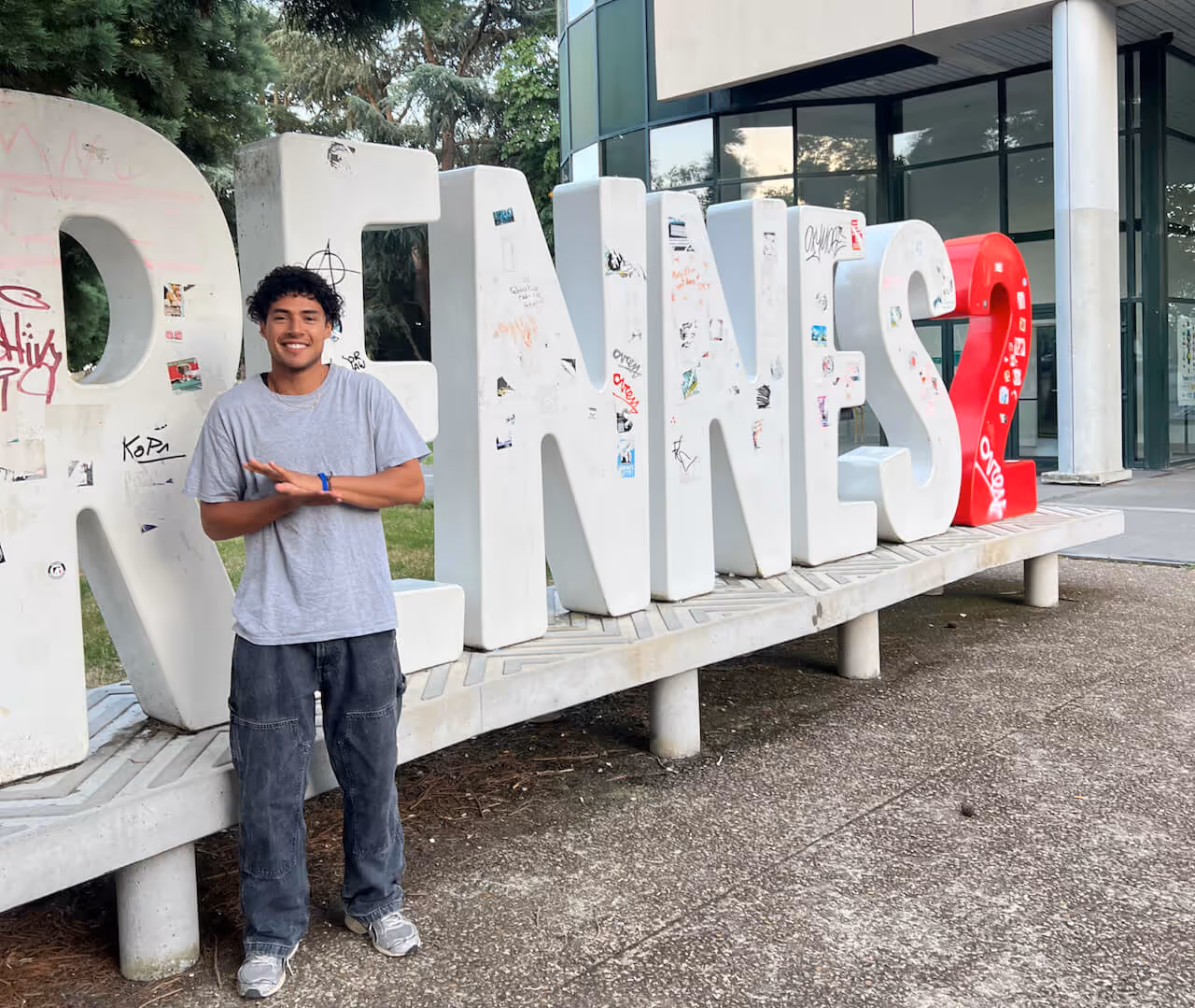A large group of campers gathers around a bonfire in the woods for cultural exchange.