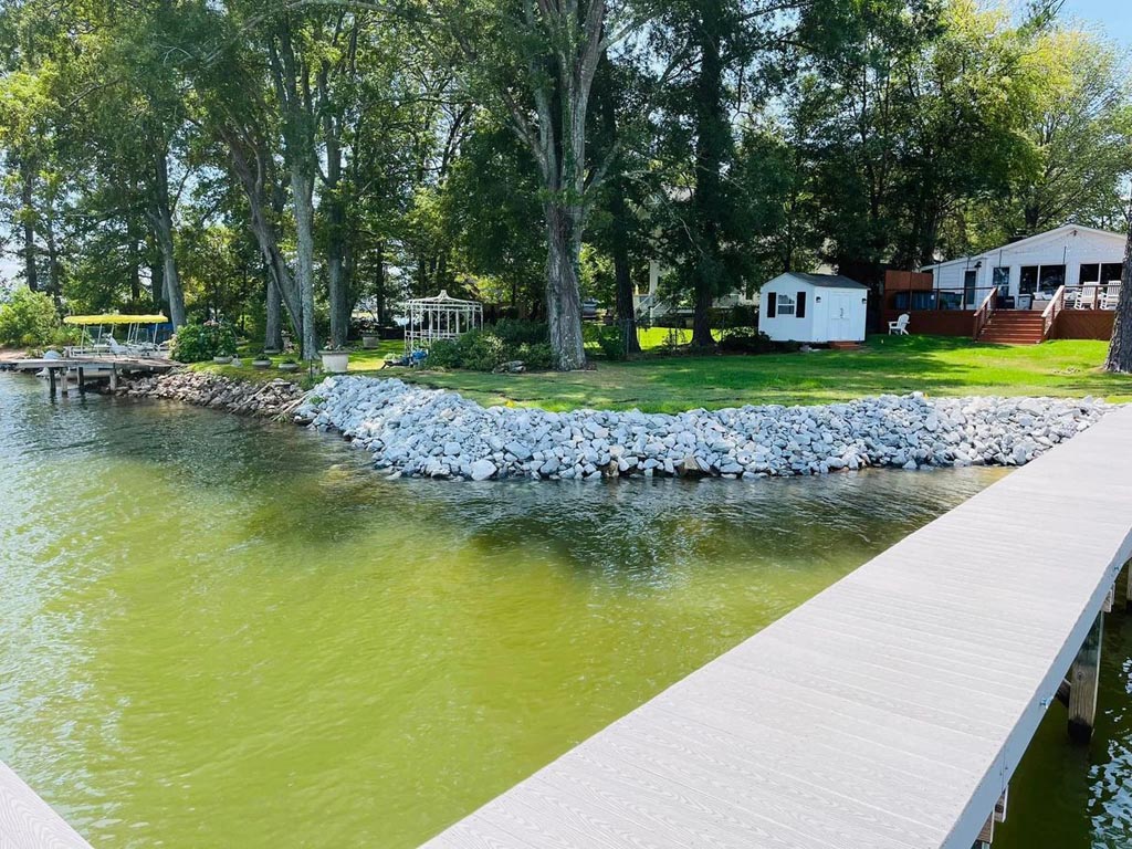 A very clean looking wall of white rocks edging a shoreline with a home and buildings in the background.