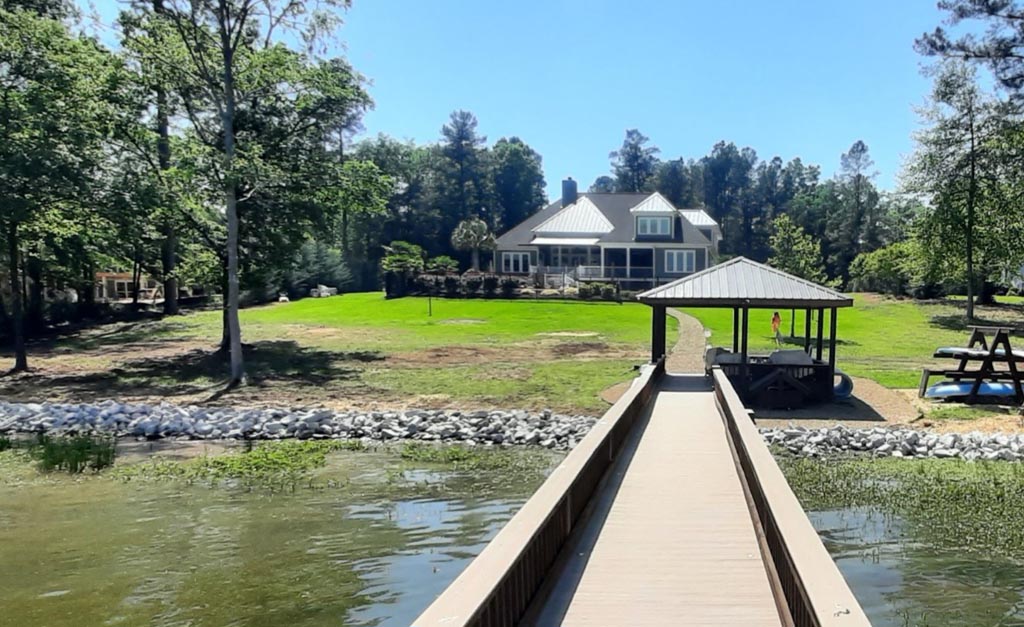 A clean shoreline of white rocks, accenting a home from viewers on the lake's dock.