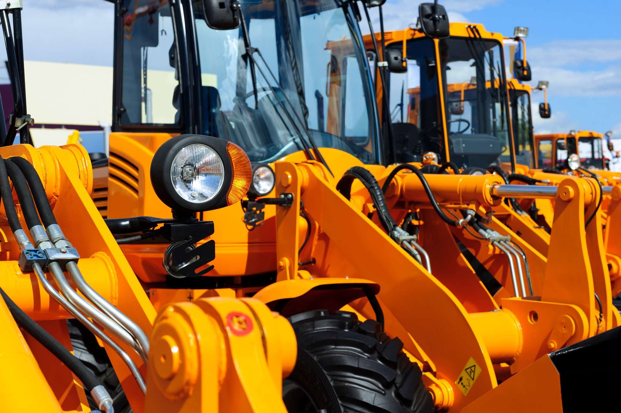 Row of bright yellow construction loaders with hydraulic arms and enclosed cabs