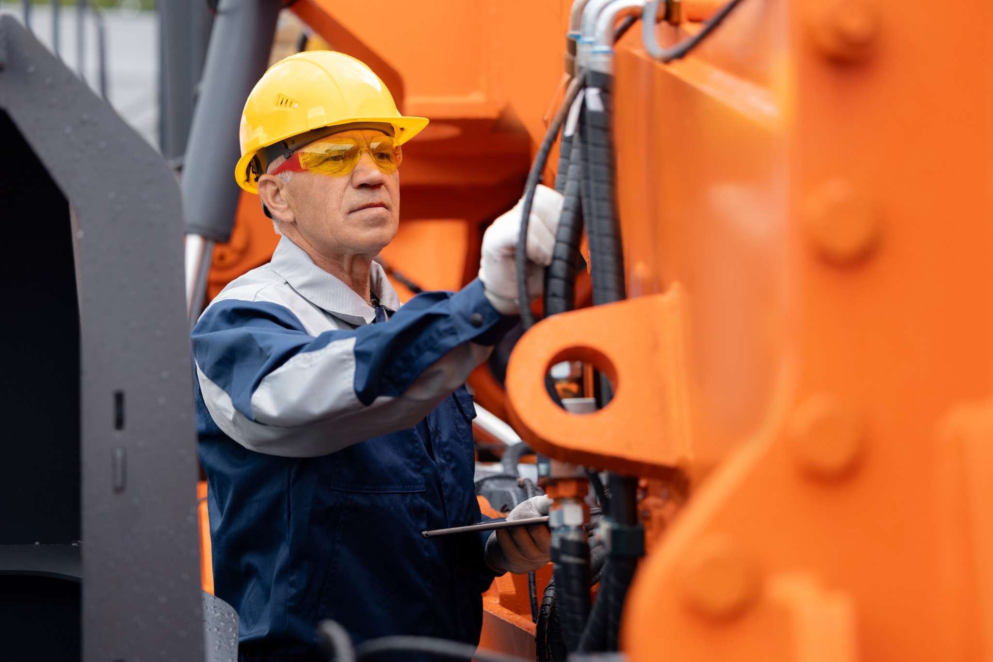 Engineer in safety gear inspecting hydraulic hoses on heavy machinery