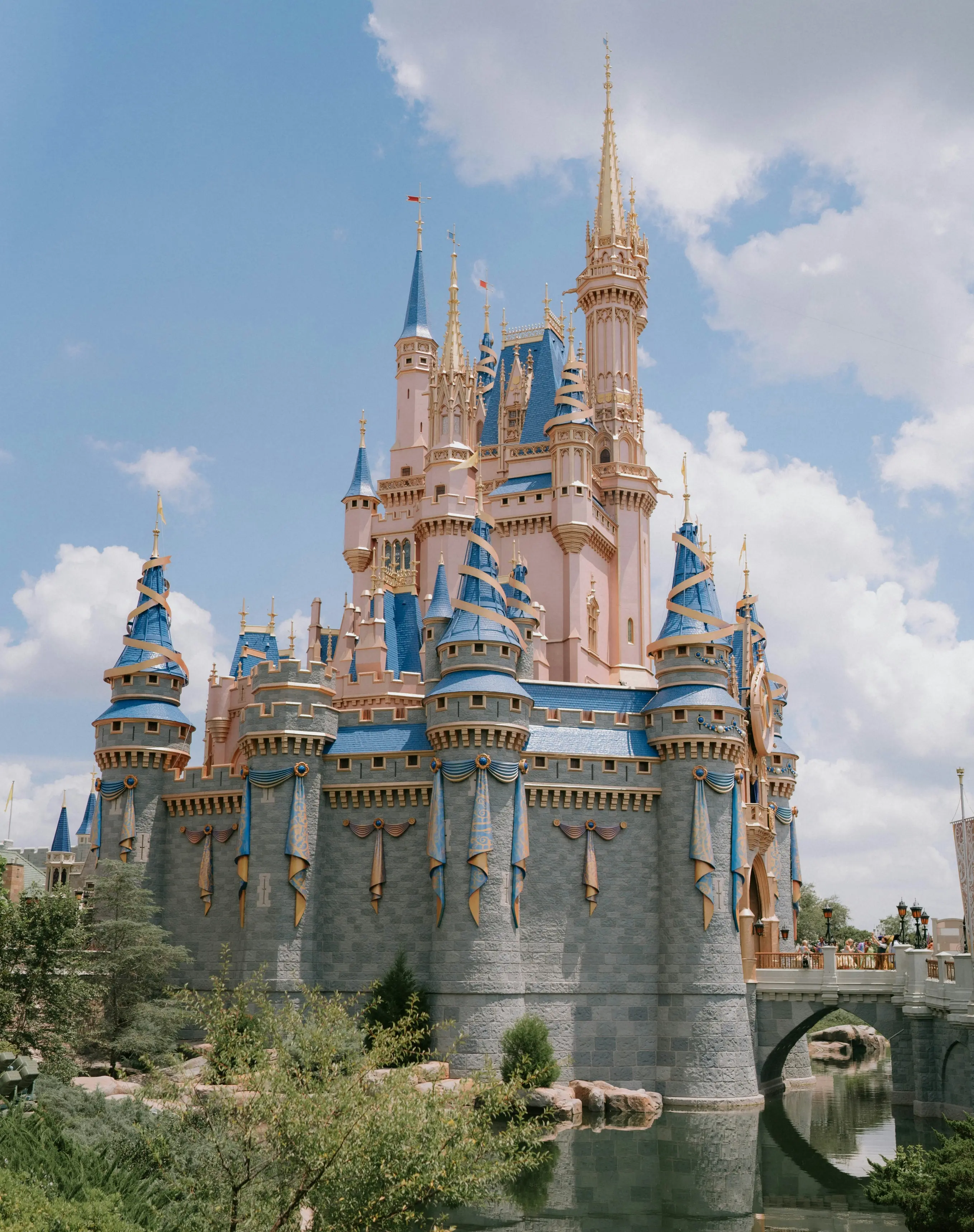 Orlando's Cindrella castle with pink walls and blue spires, set against a vibrant blue sky with fluffy clouds. The scene is whimsical and enchanting.