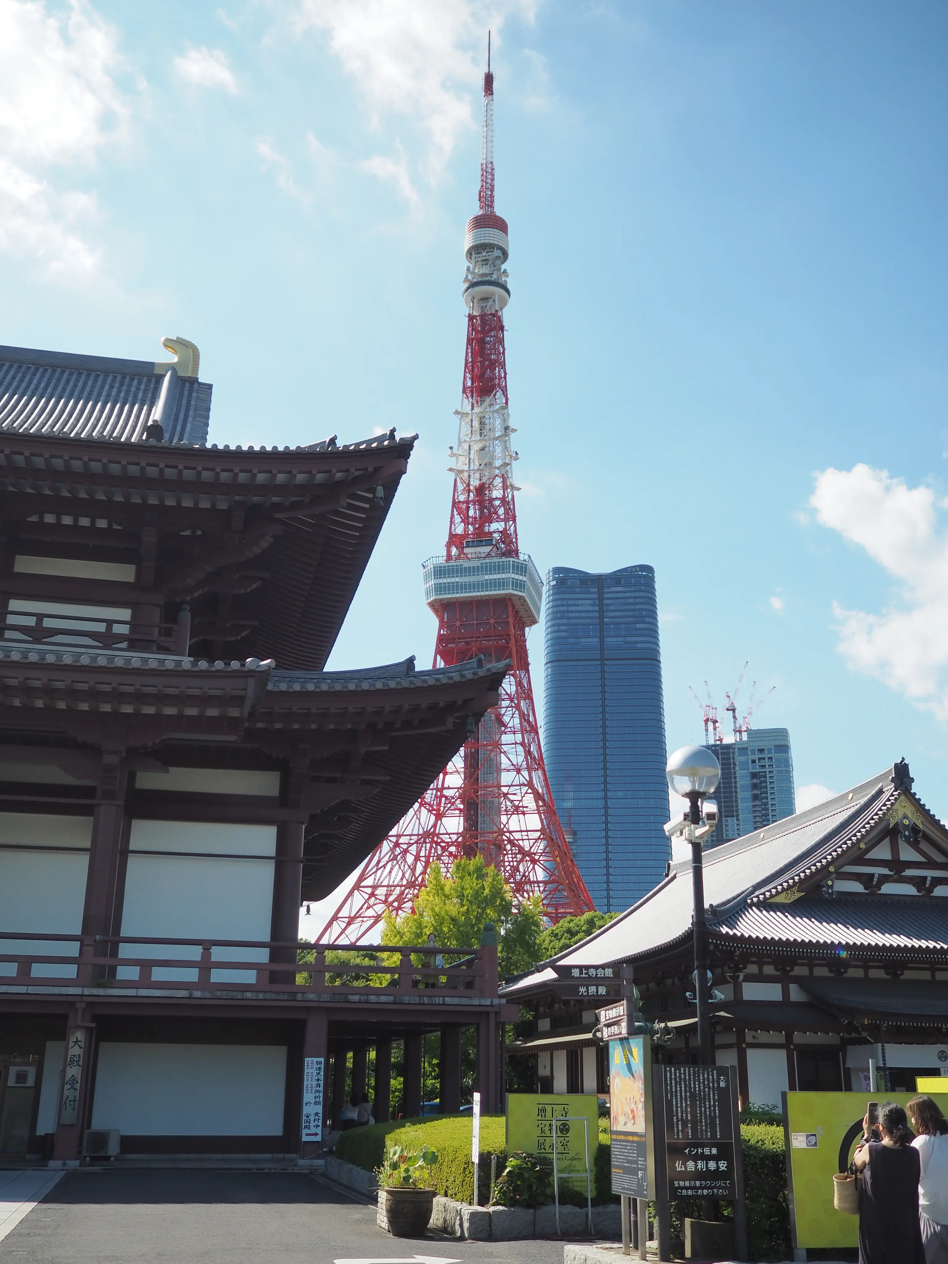 Traditional Japanese temple roofs juxtaposed with Tokyo Tower and modern skyscrapers under a bright blue sky, conveying a blend of history and modernity.