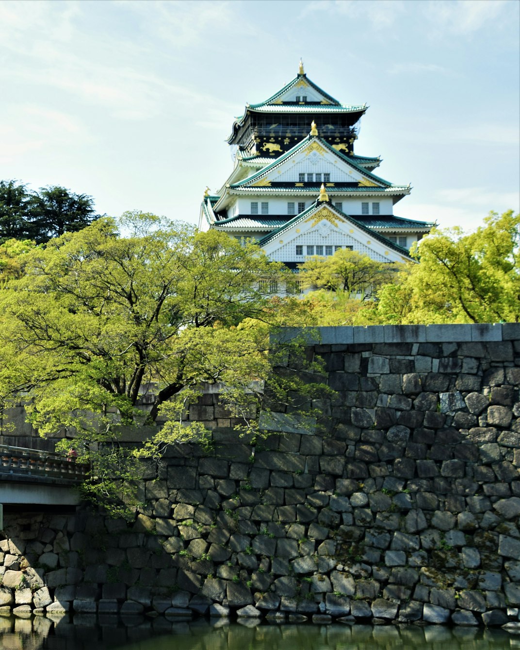 Osaka Castle rising above its stone walls and green trees under a blue sky