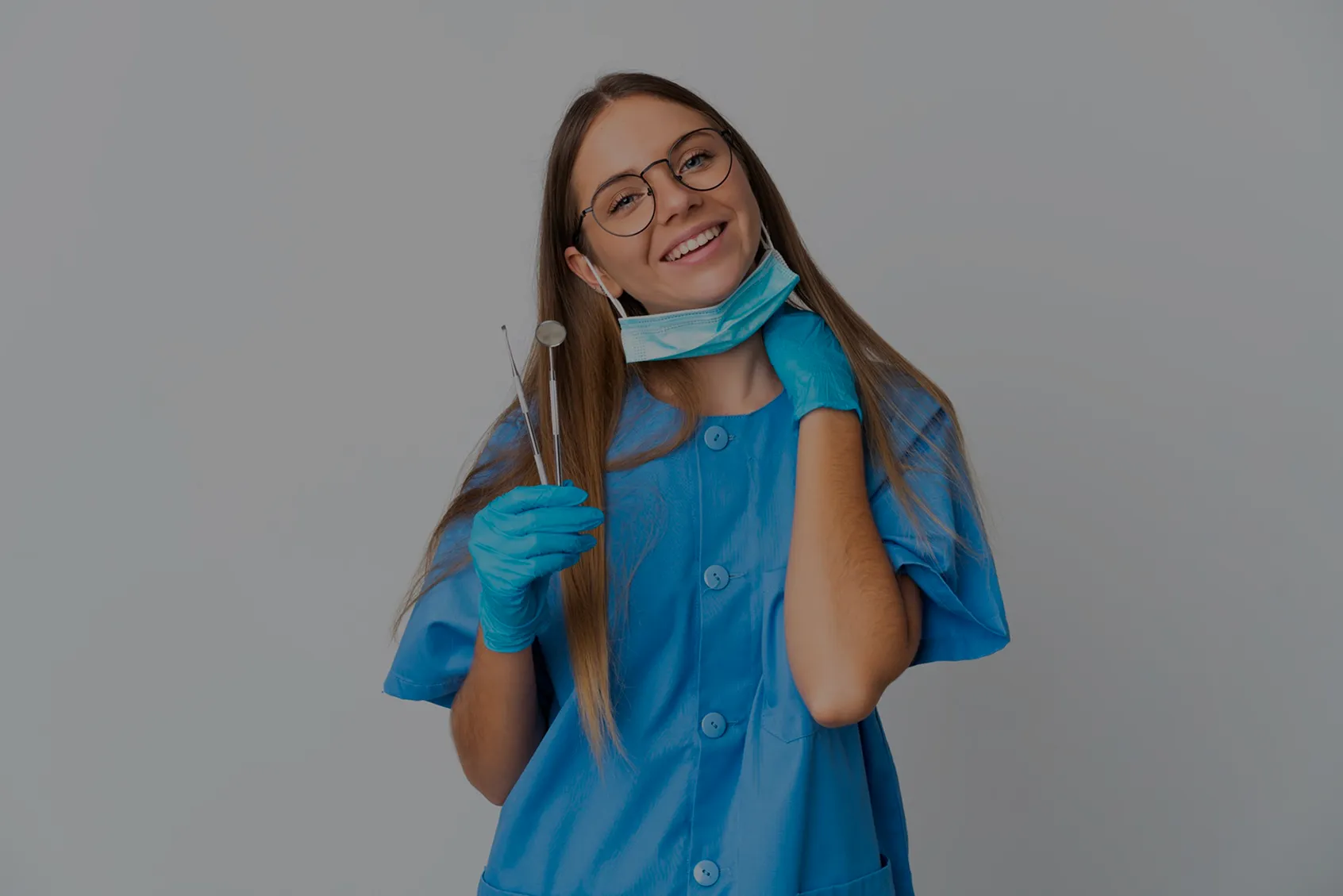 Forside bildee av til klinikkvalg av en smilende tannlege iført blå uniform, munnbind og hansker, holder tannlegeverktøy foran en nøytral bakgrunn.