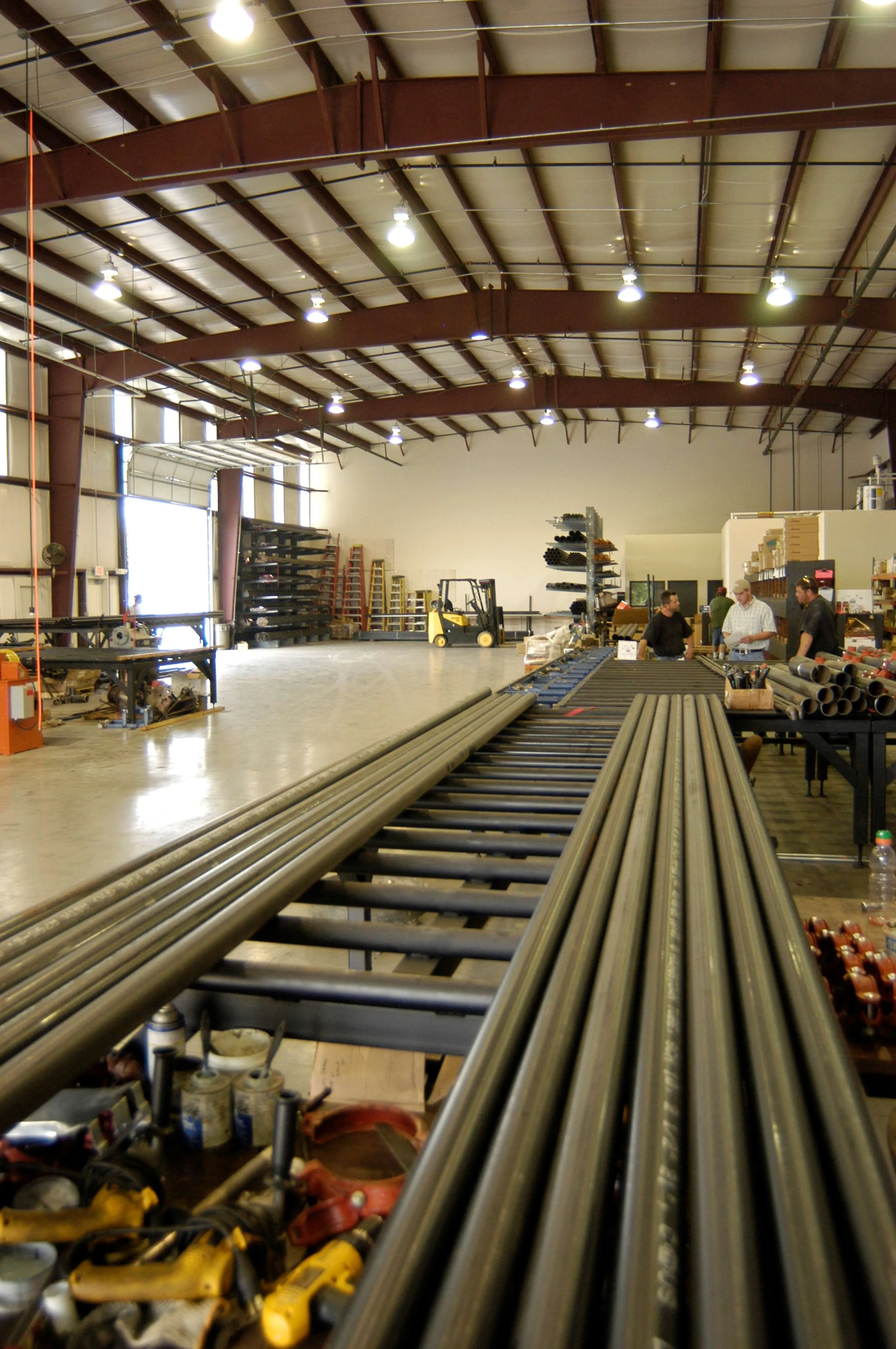 Industrial workspace with metal pipes and workers collaborating in a well-lit fabrication shop.
