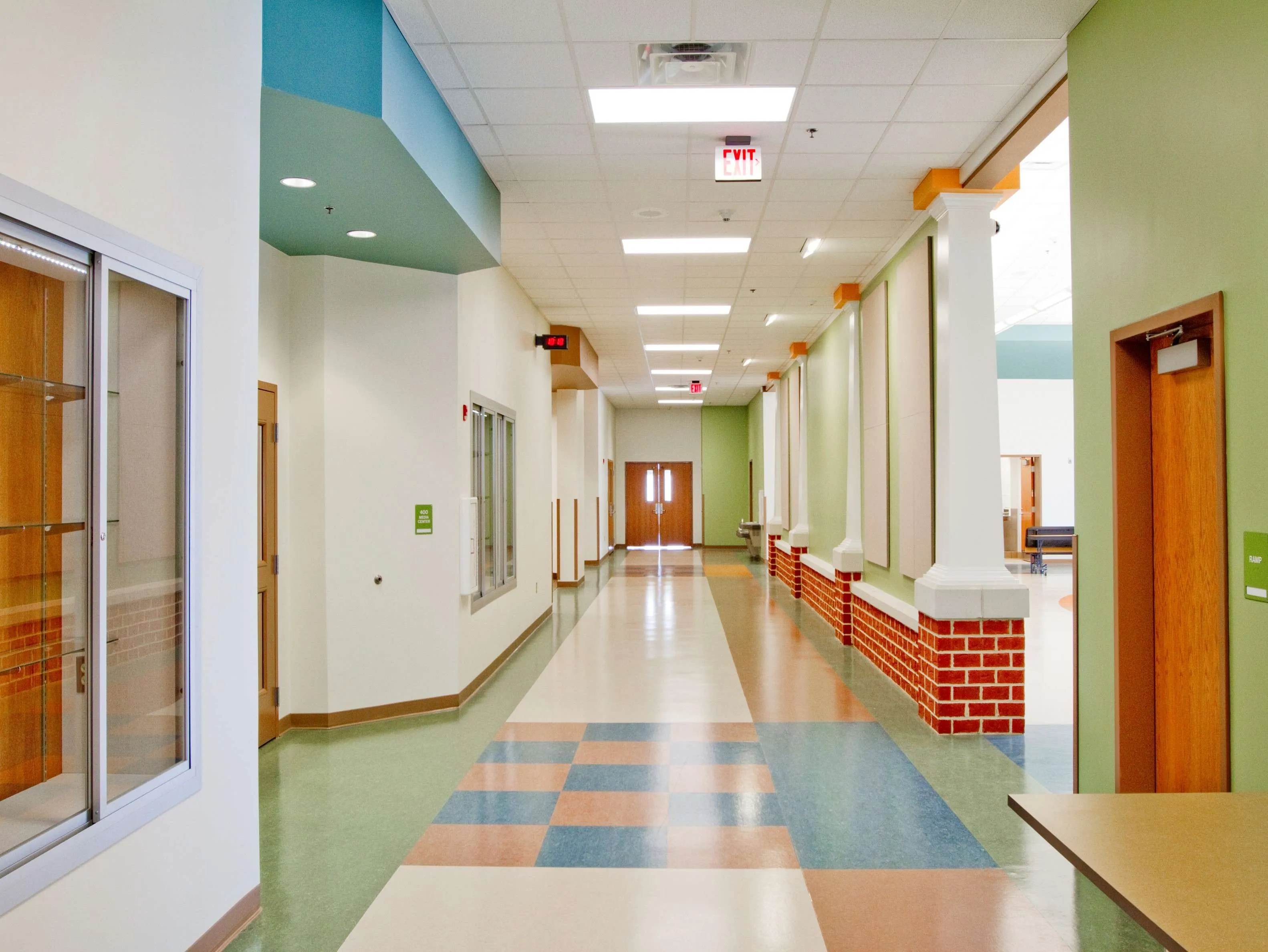 Bright and spacious hallway in a modern school, featuring colorful flooring and accessible signage.
