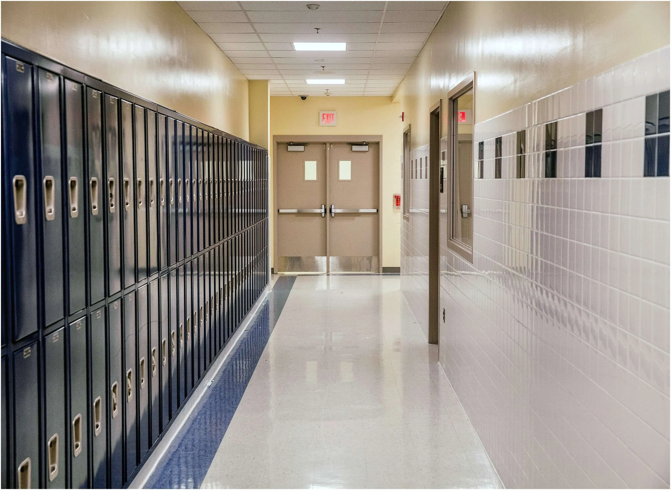 A school hallway featuring blue lockers on the left side and double doors at the end.
