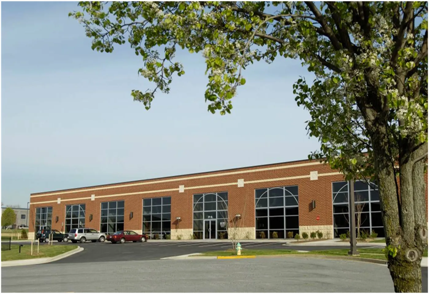 A modern brick building with large windows and a landscaped parking area.
