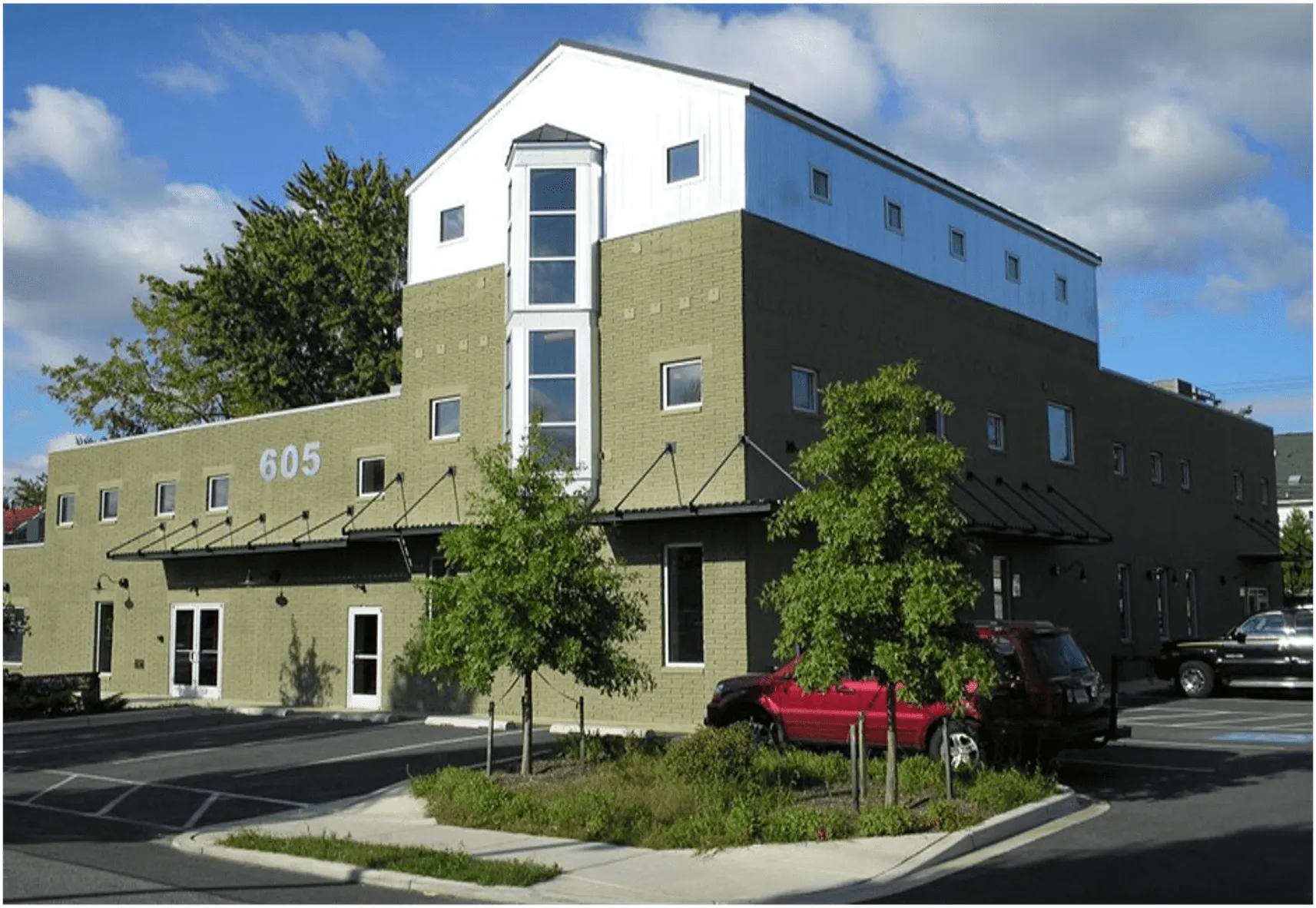 Modern green building exterior with large windows and parking area, located at 605.
