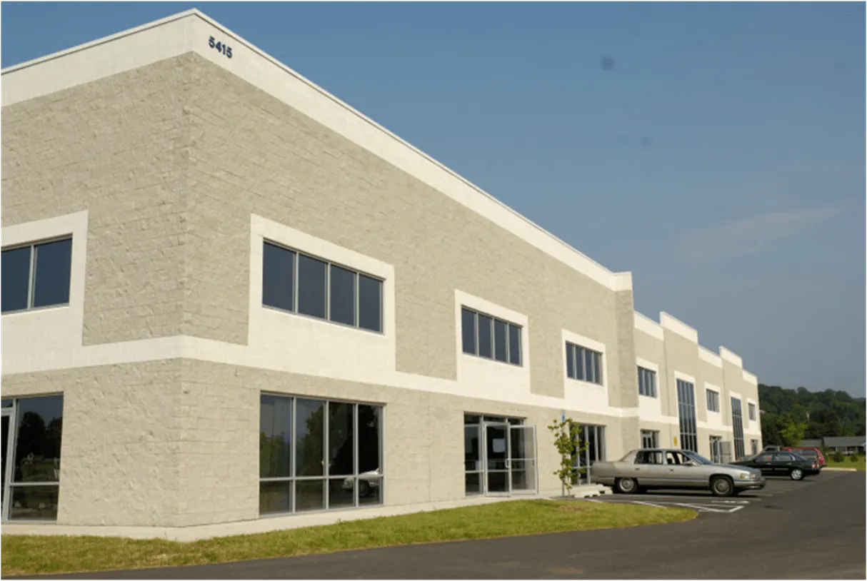 Modern warehouse building exterior with large windows and parking area.
