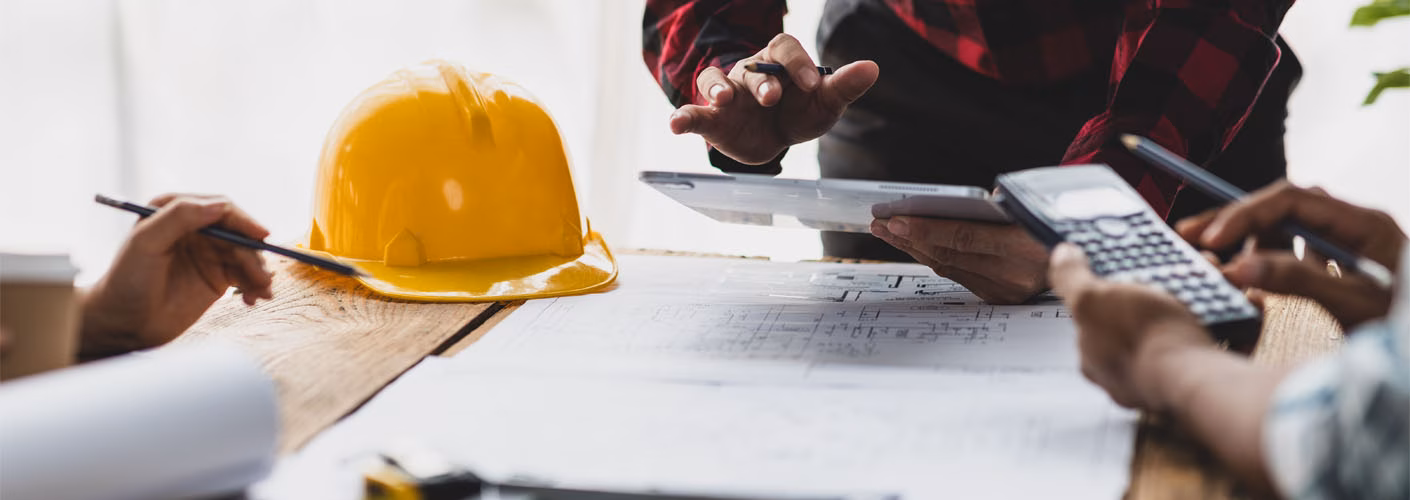 People around a table with architects drawings and construction hard hat and a calculator