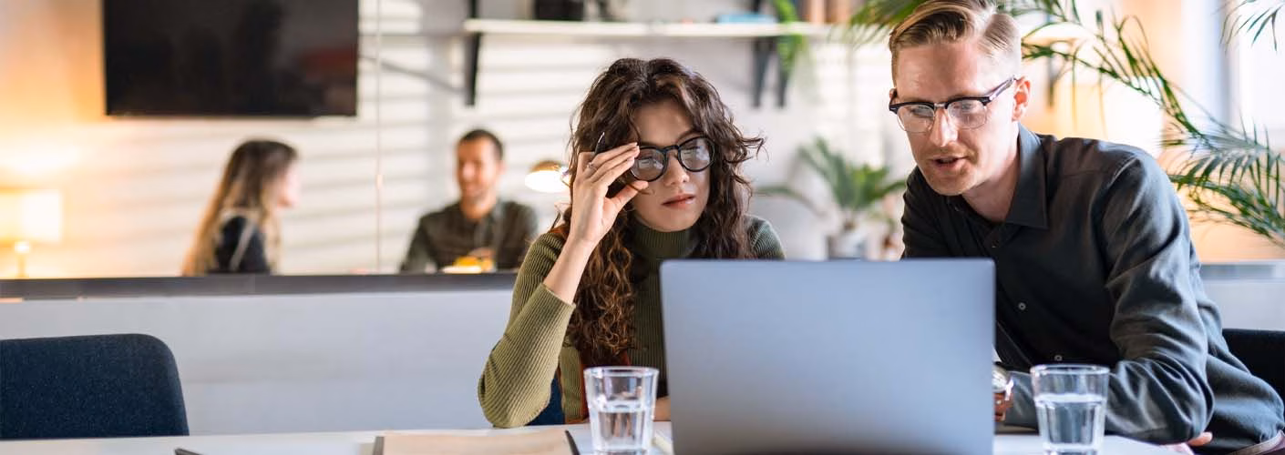 Two people sat at a desk with a clipboard looking at a laptop
