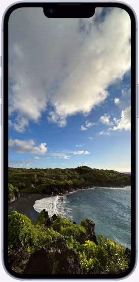 Strand mit schwarzem Sand, umgeben von grüner Vegetation und felsiger Küste unter blauem Himmel mit Wolken, angezeigt auf einem Smartphone-Bildschirm.