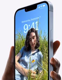 Hand hält Smartphone mit Bild eines jungen Mannes in blauer Kleidung, der in einem Grasfeld sitzt.