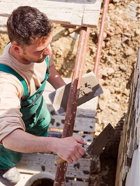 Un ouvrier en salopette verte travaillant sur une structure en bois