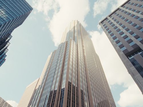View looking up at tall glass and steel skyscrapers against a blue sky with clouds.